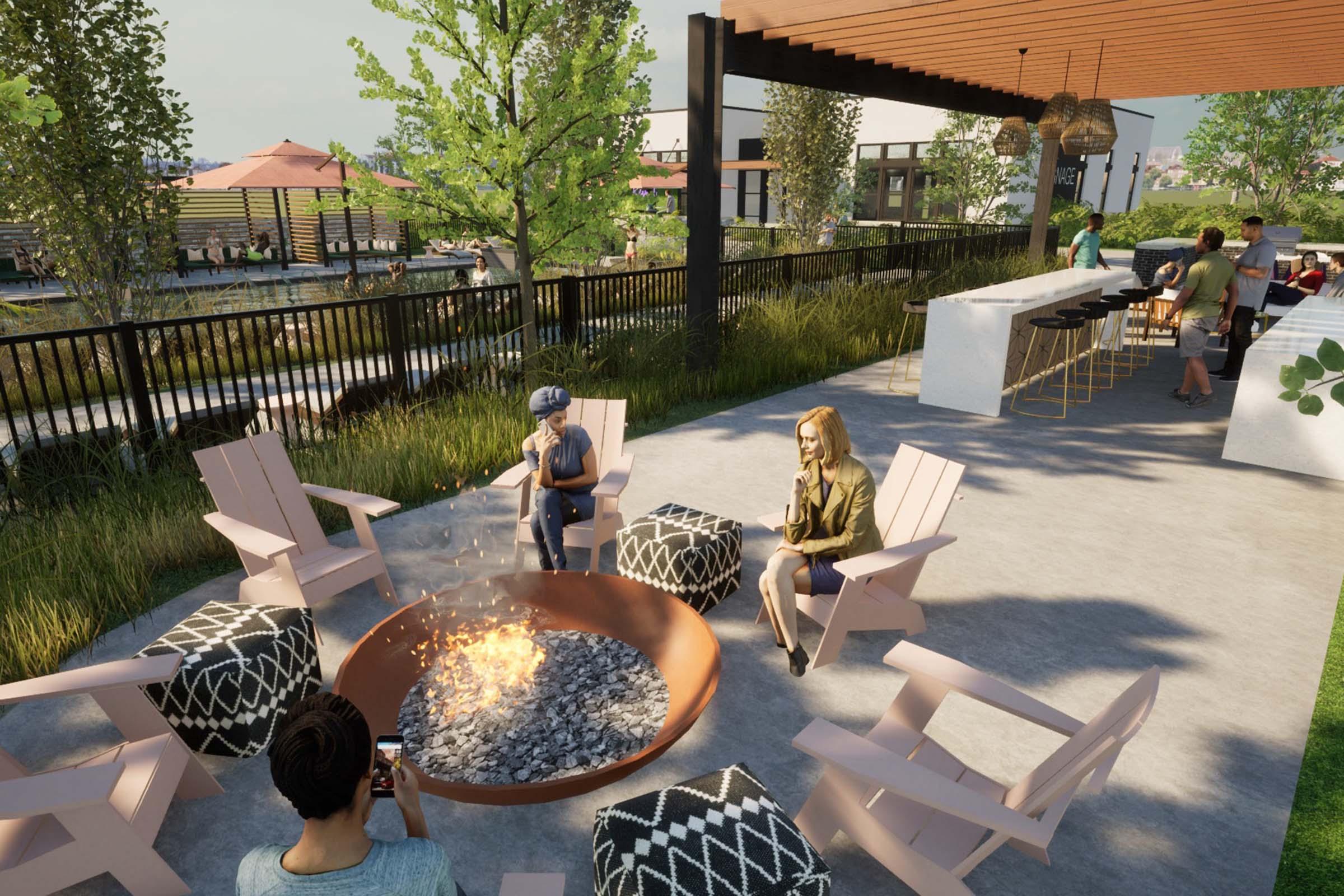 A cozy outdoor lounge area features a circular fire pit surrounded by pink adirondack chairs and patterned ottomans. People relax, with one person taking a photo, while others enjoy the ambiance. In the background, there are trees and a patio with seating under a roof, creating a welcoming social space.