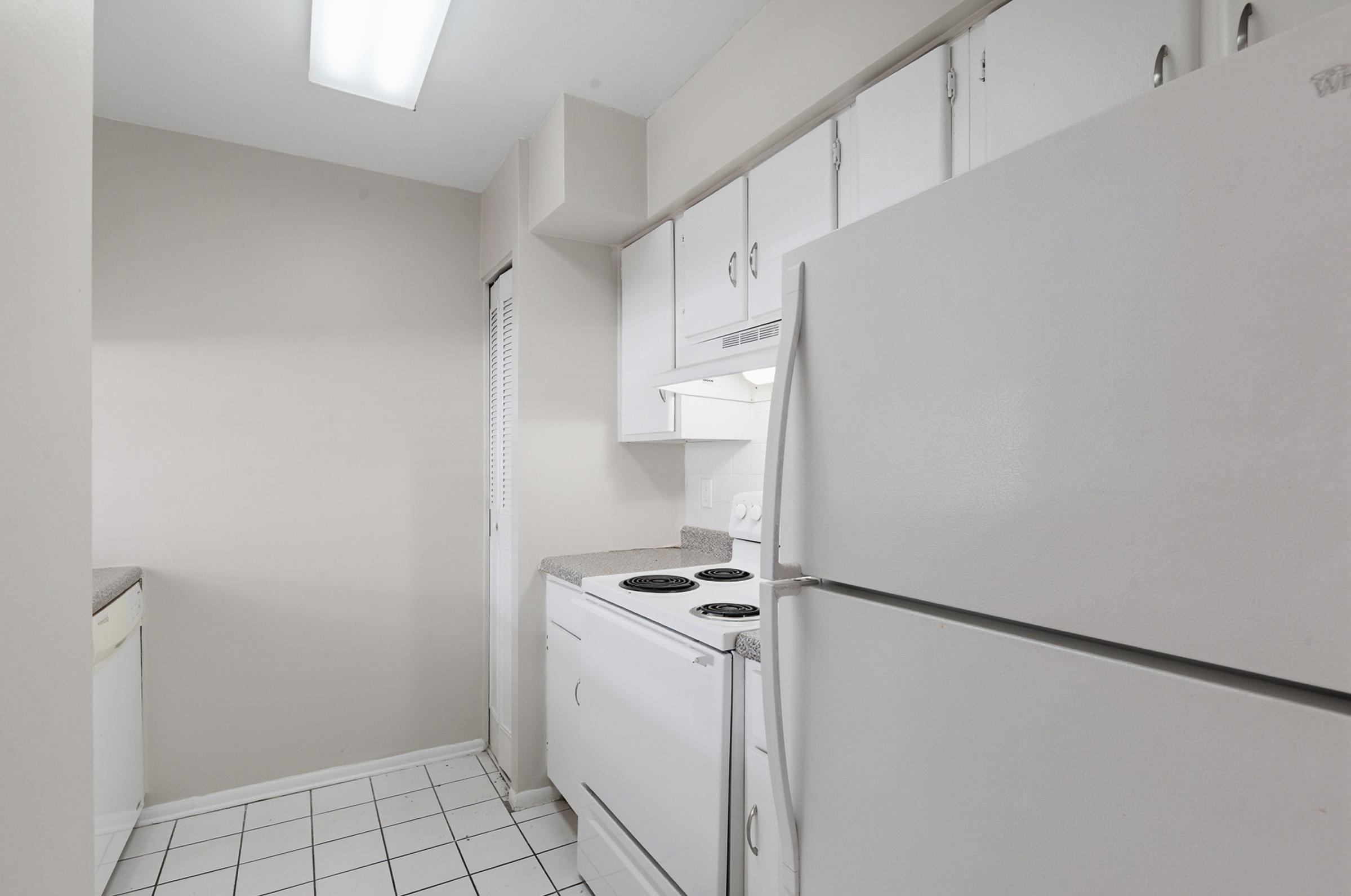 A compact kitchen featuring white cabinetry, a refrigerator, an electric stove with a flat surface, and a neutral color scheme. The space includes a tiled floor and a window, maximizing light and functionality in the setup.