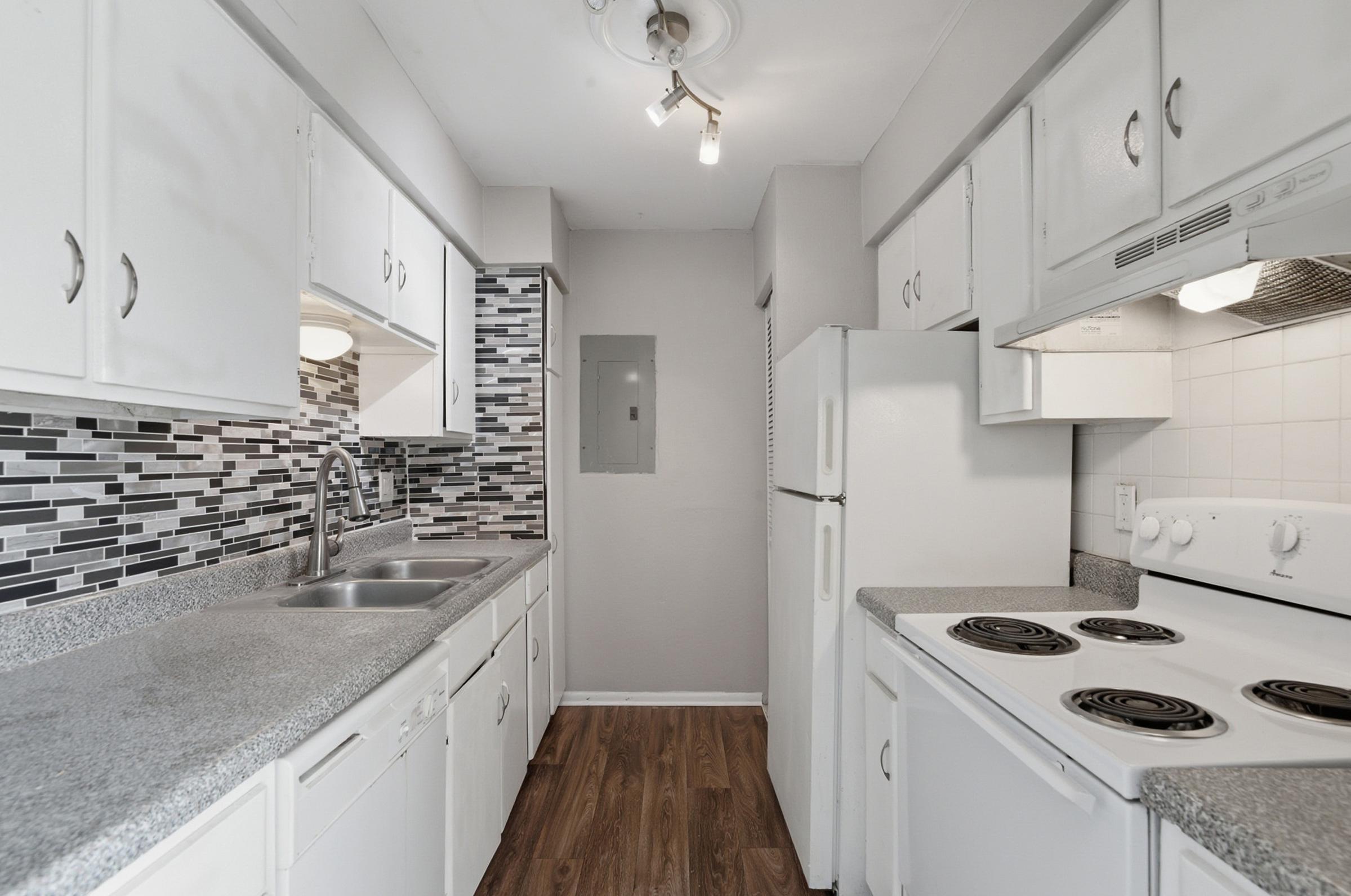 Modern kitchen featuring white cabinetry, a gray countertop, and a stylish backsplash of black and white tiles. The kitchen includes a double sink, a refrigerator, and a stove with an oven. Natural light illuminates the space, highlighting the clean and organized layout.