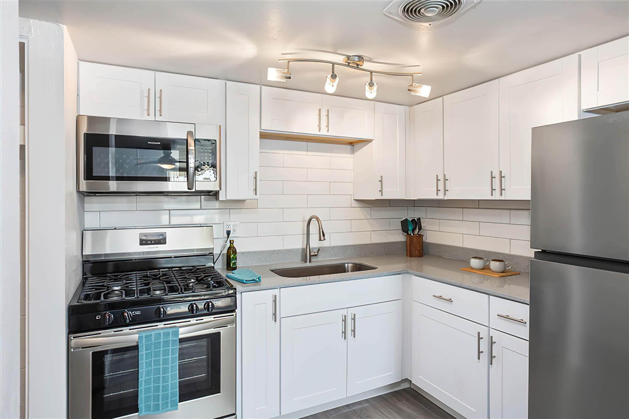 Upscale kitchen with stainless steel appliances, white shaker cabinets, and grey quartz countertops