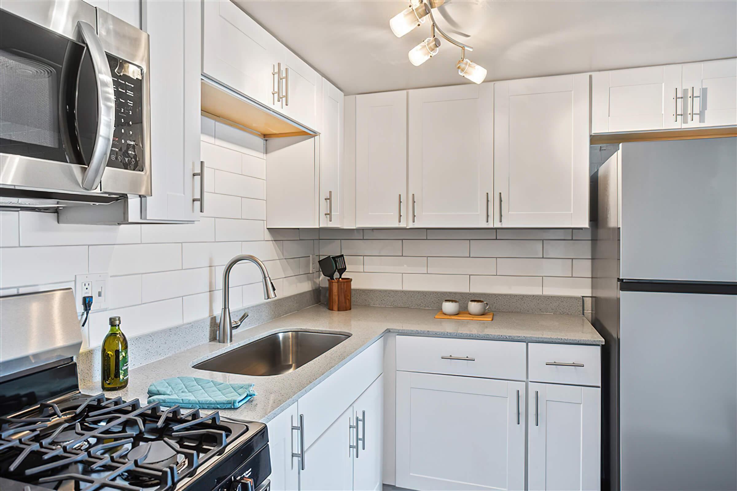 Upscale kitchen with stainless steel appliances, white shaker cabinets, and grey quartz countertops