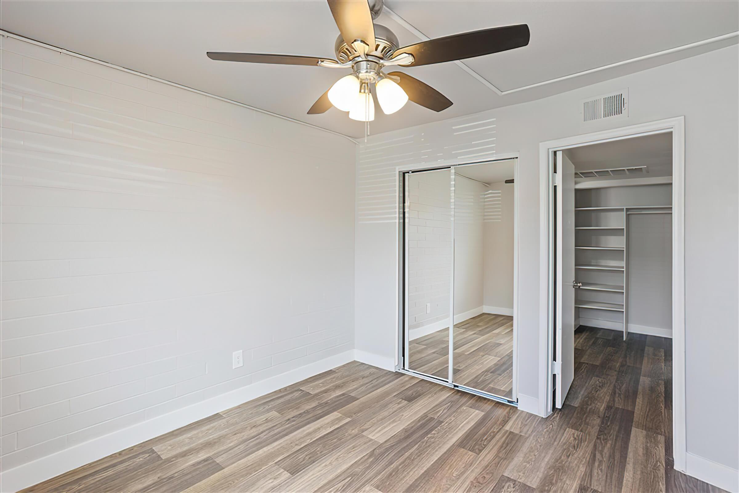 Large empty bedroom with view of a ceiling fan, mirrored closets, and a large walk in closet