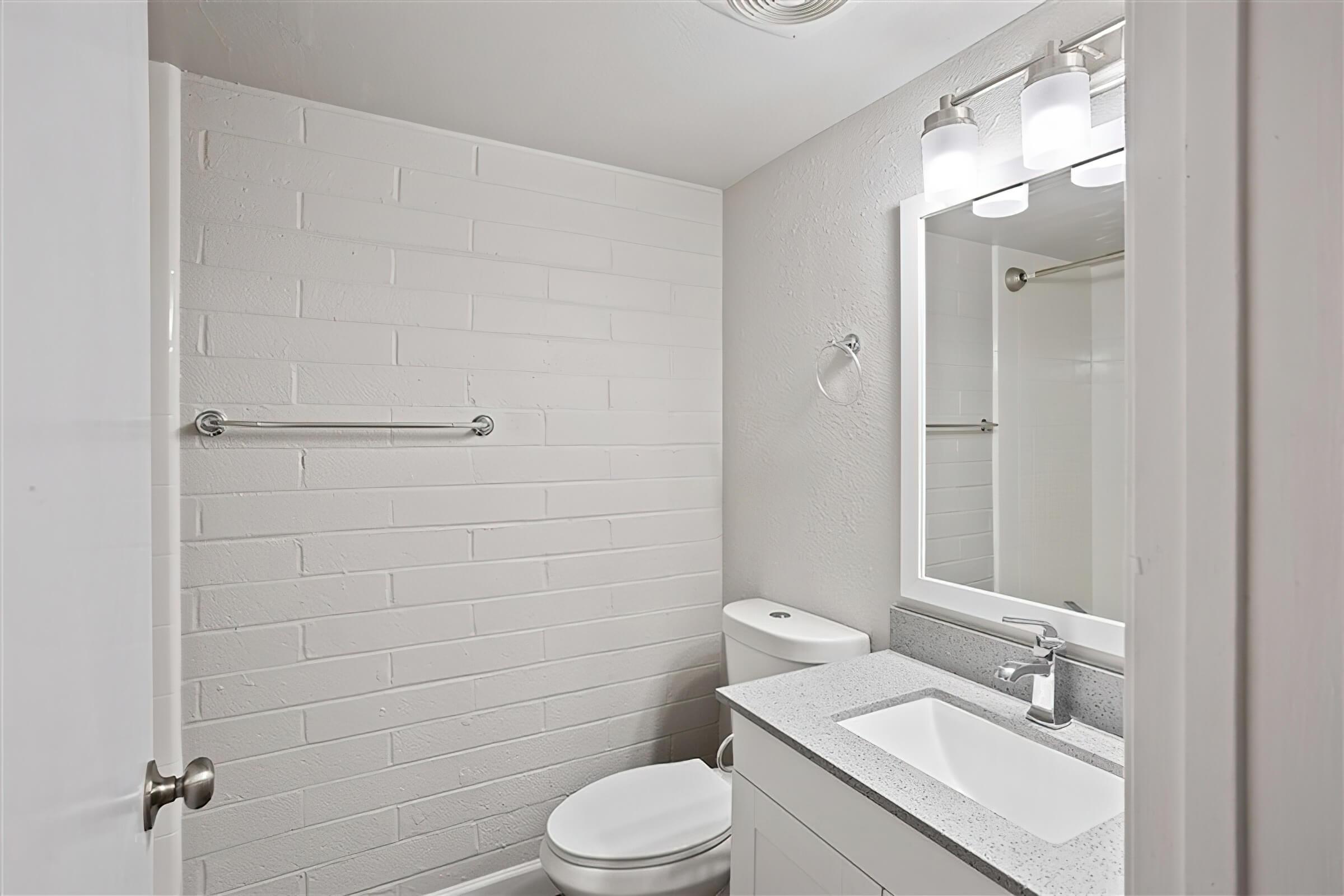 Modern renovated bathroom space with a brick wall, toilet, and grey mirrored vanity sink