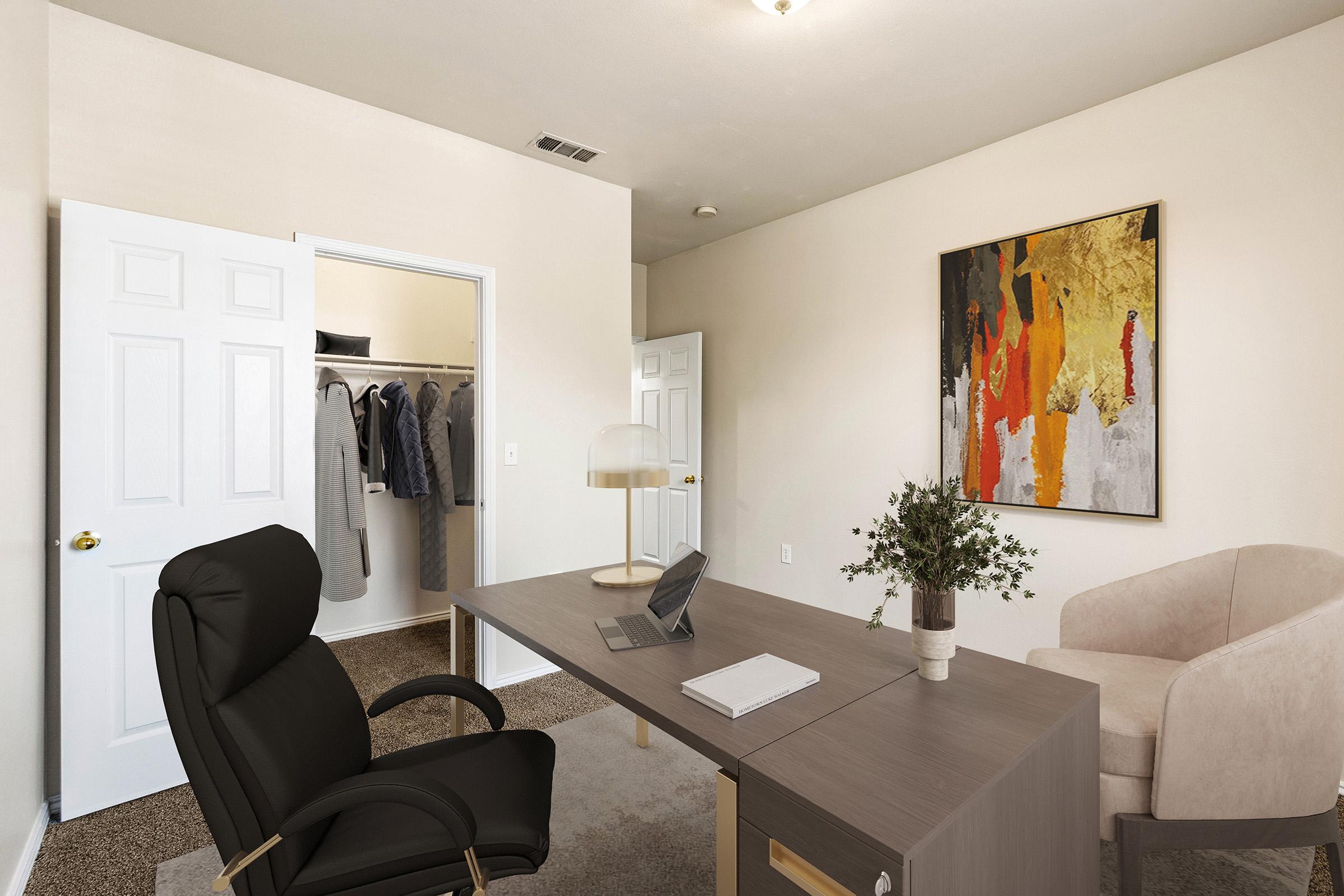 A modern office space featuring a black ergonomic chair facing a sleek gray desk with a tablet and a notebook. In the background, there is an open closet with clothes hanging, and two white doors leading to separate rooms. A beige armchair and a decorative artwork with vibrant colors adorn the wall.