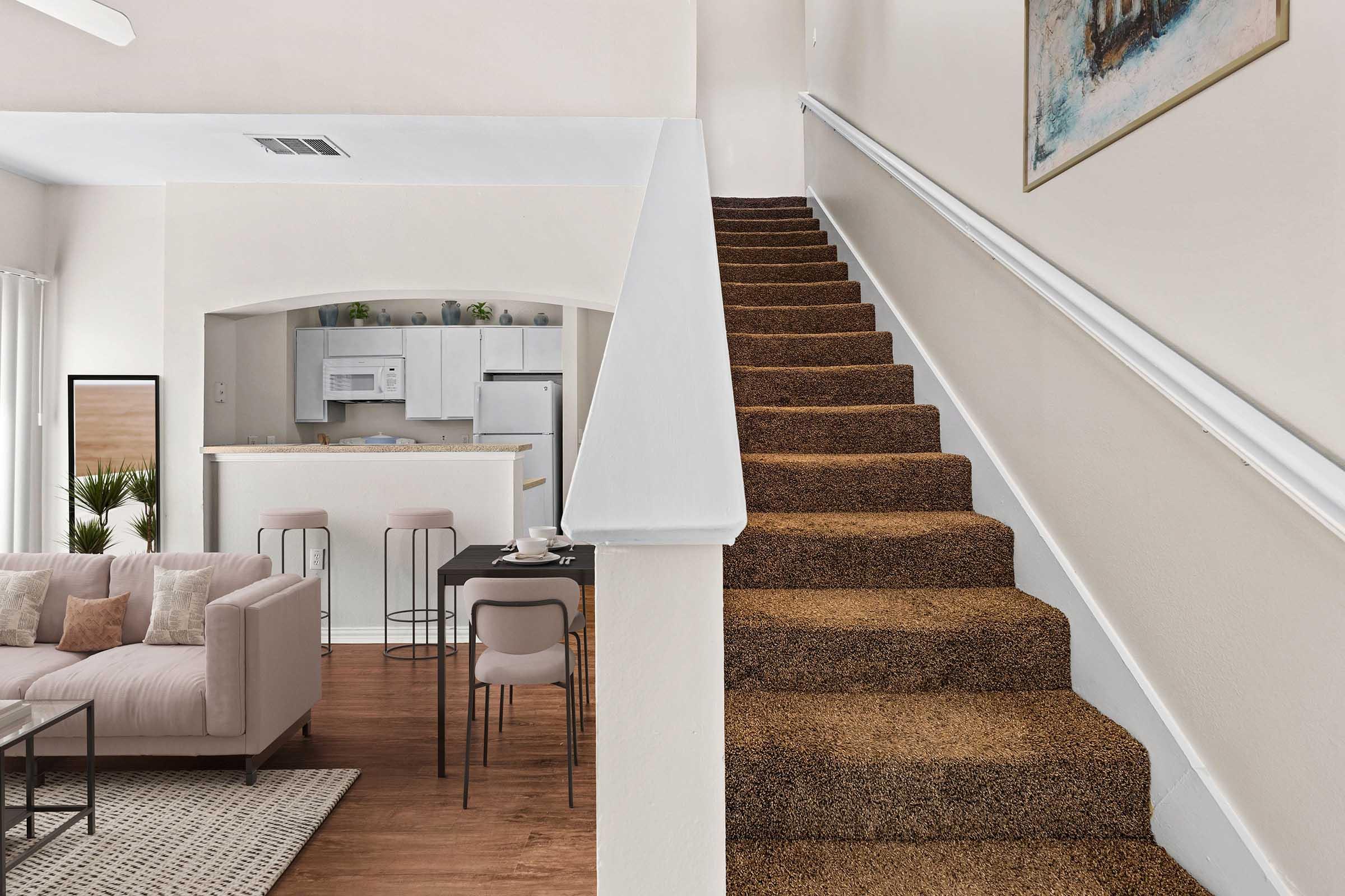 A cozy interior of a home featuring a staircase with carpet, leading to an upper level. The open living space includes a modern couch, a dining area with chairs, and a kitchen visible in the background. Warm colors and minimalistic decor create a welcoming atmosphere.