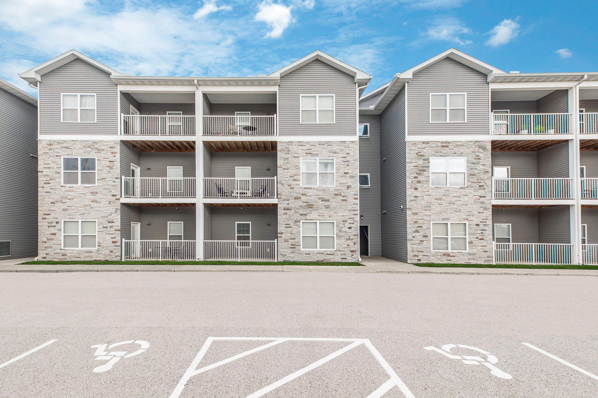 Exterior view of three-story apartments and parking area at The Groves on Devils Glen in Bettendorf, IA