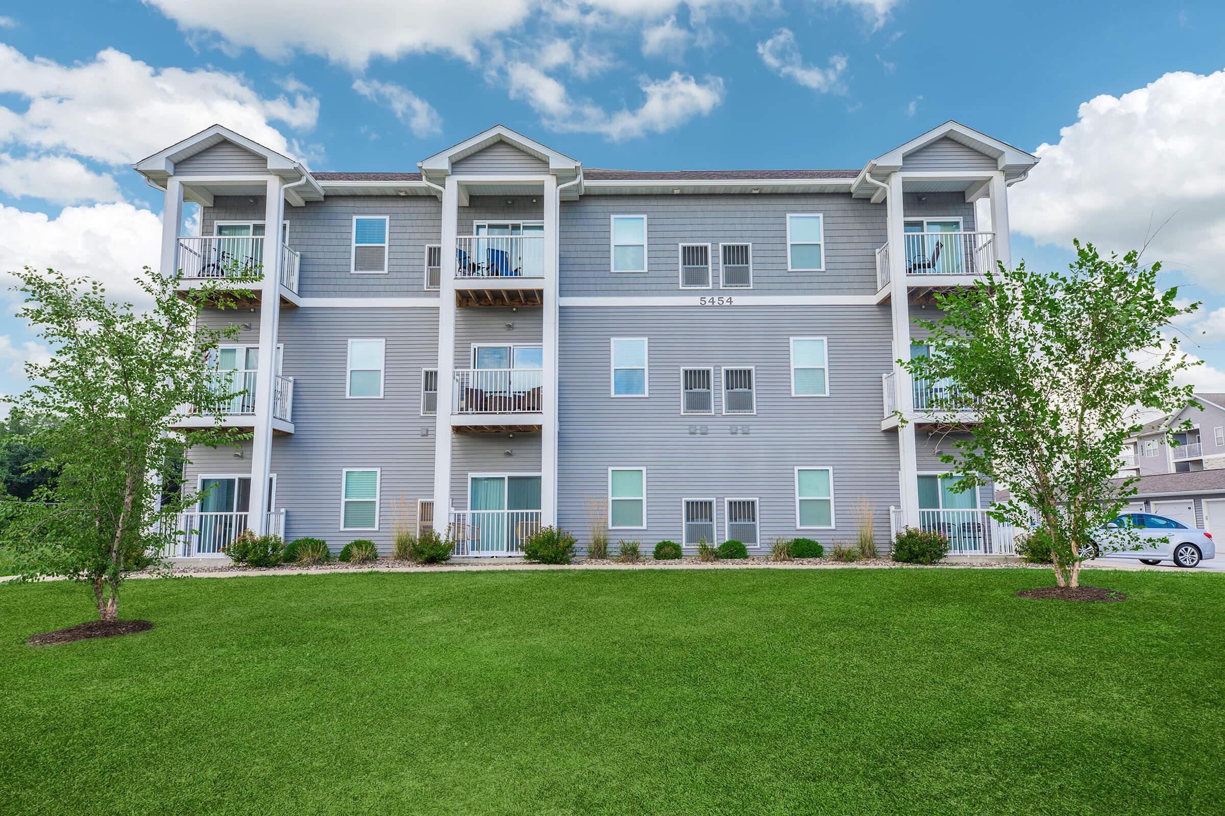 Exterior view of apartments with balconies and green lawn at The Groves on Devils Glen in Bettendorf, IA