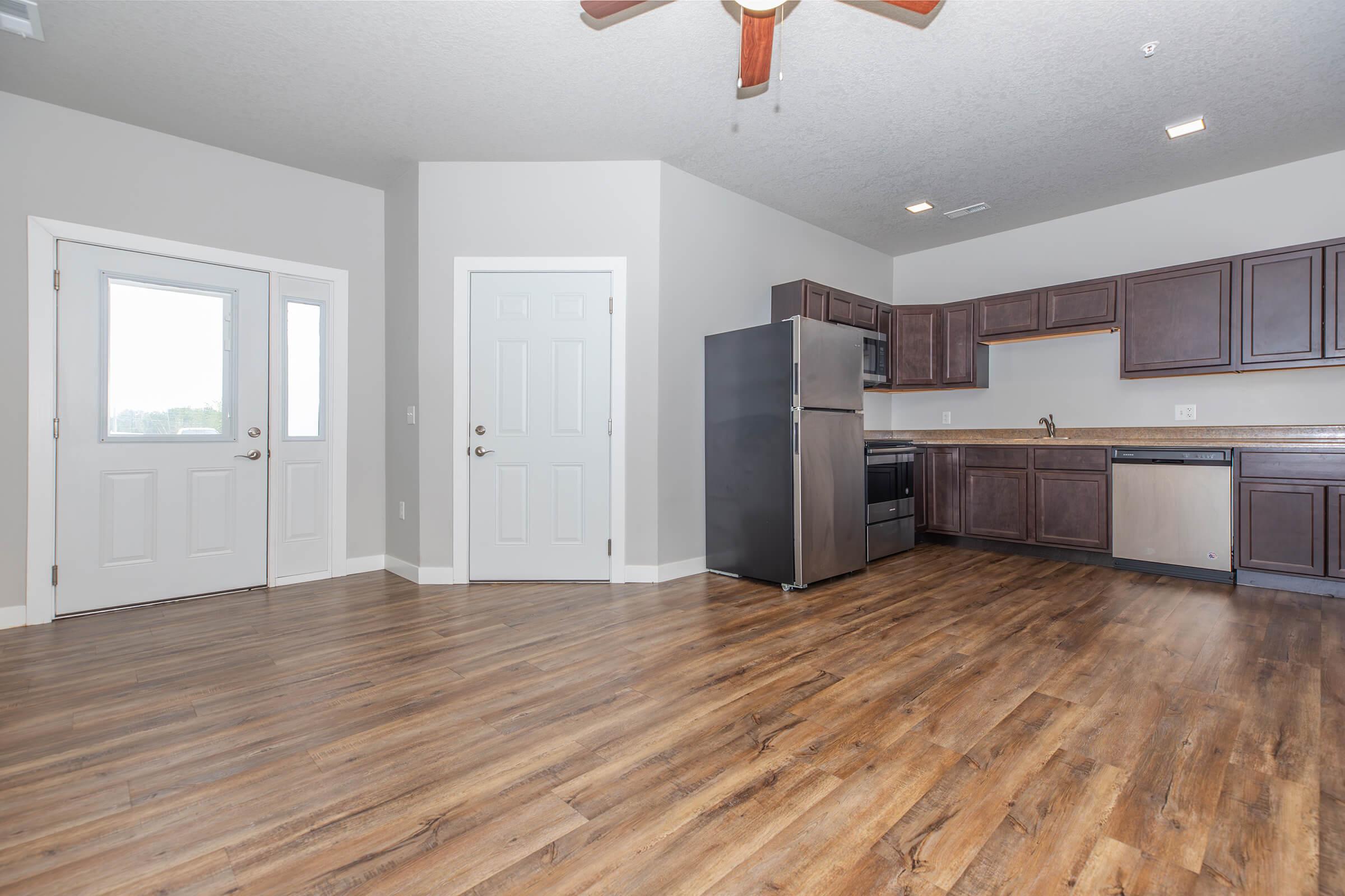 Open kitchen and dining area with stainless steel appliances and wood-style flooring at The Groves on Devils Glen in Bettendorf, IA