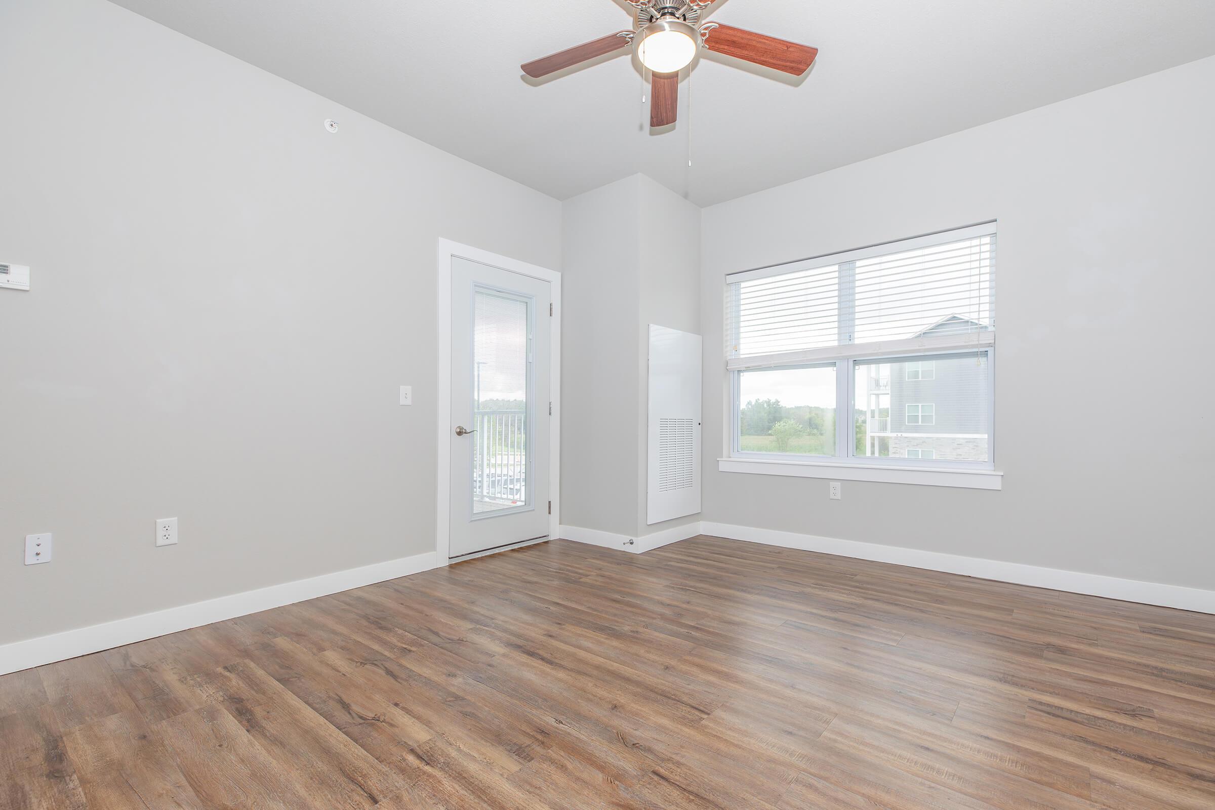 Bright living room with large windows, ceiling fan, and wood-style floors at The Groves on Devils Glen in Bettendorf, IA