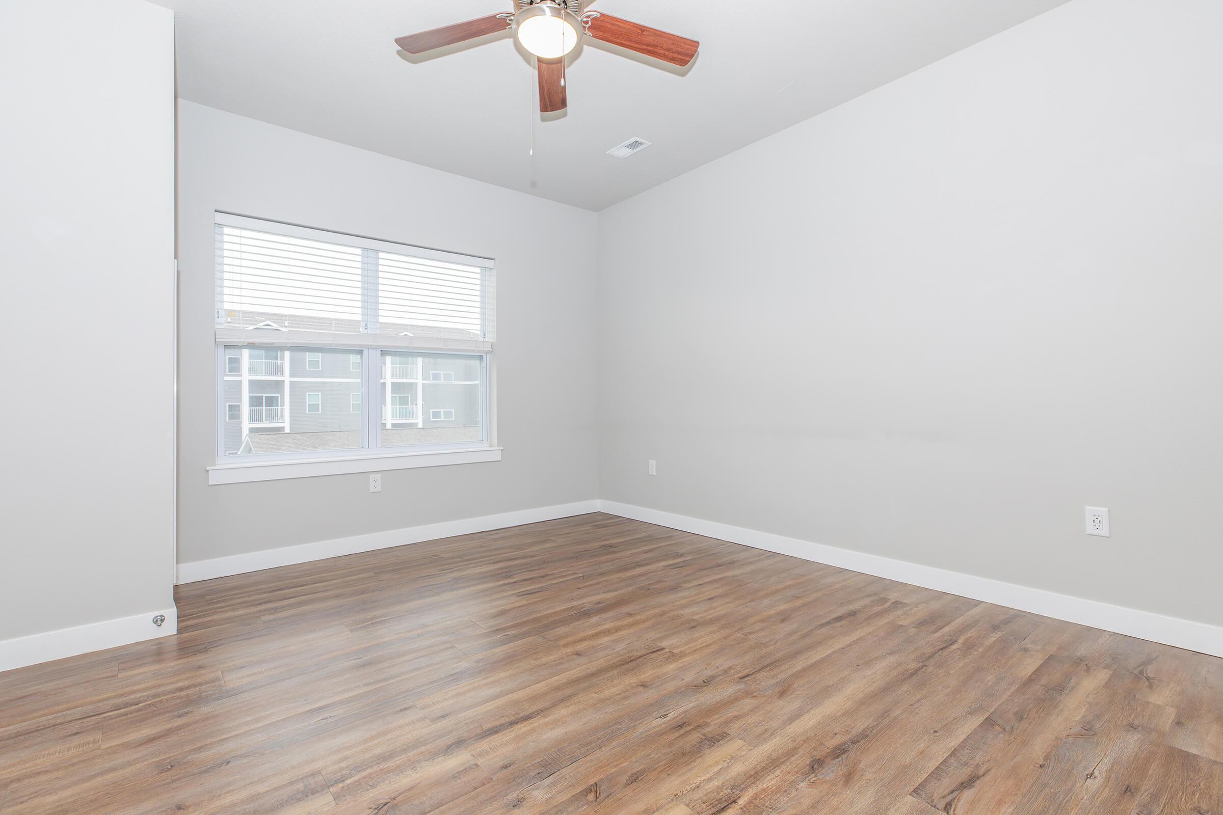 Spacious bedroom with ceiling fan and wood-style flooring at The Groves on Devils Glen in Bettendorf, IA