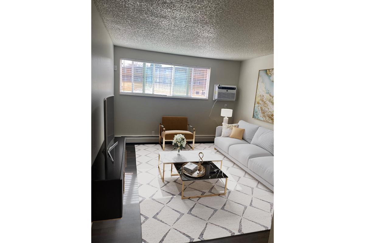 A modern living room featuring a white sofa with textured cushions, a glass coffee table on a patterned rug, and a brown armchair. Natural light streams in through large windows adorned with blinds. An air conditioning unit is visible on the wall, and there's an abstract painting on display.