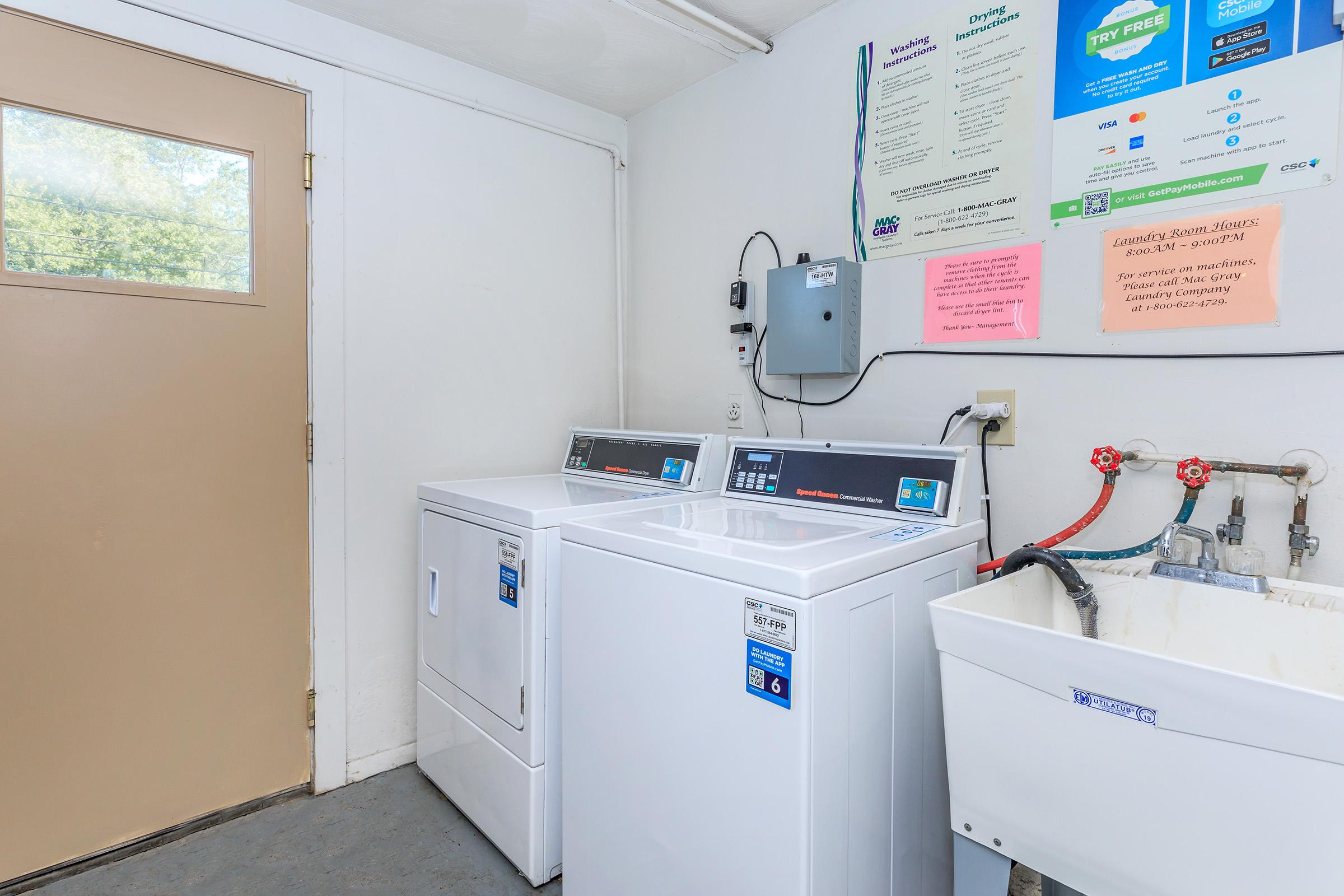 A laundry room featuring two white washing machines side by side, a utility sink, and a beige door leading outside. The walls display various informative posters and signs related to laundry instructions and services.