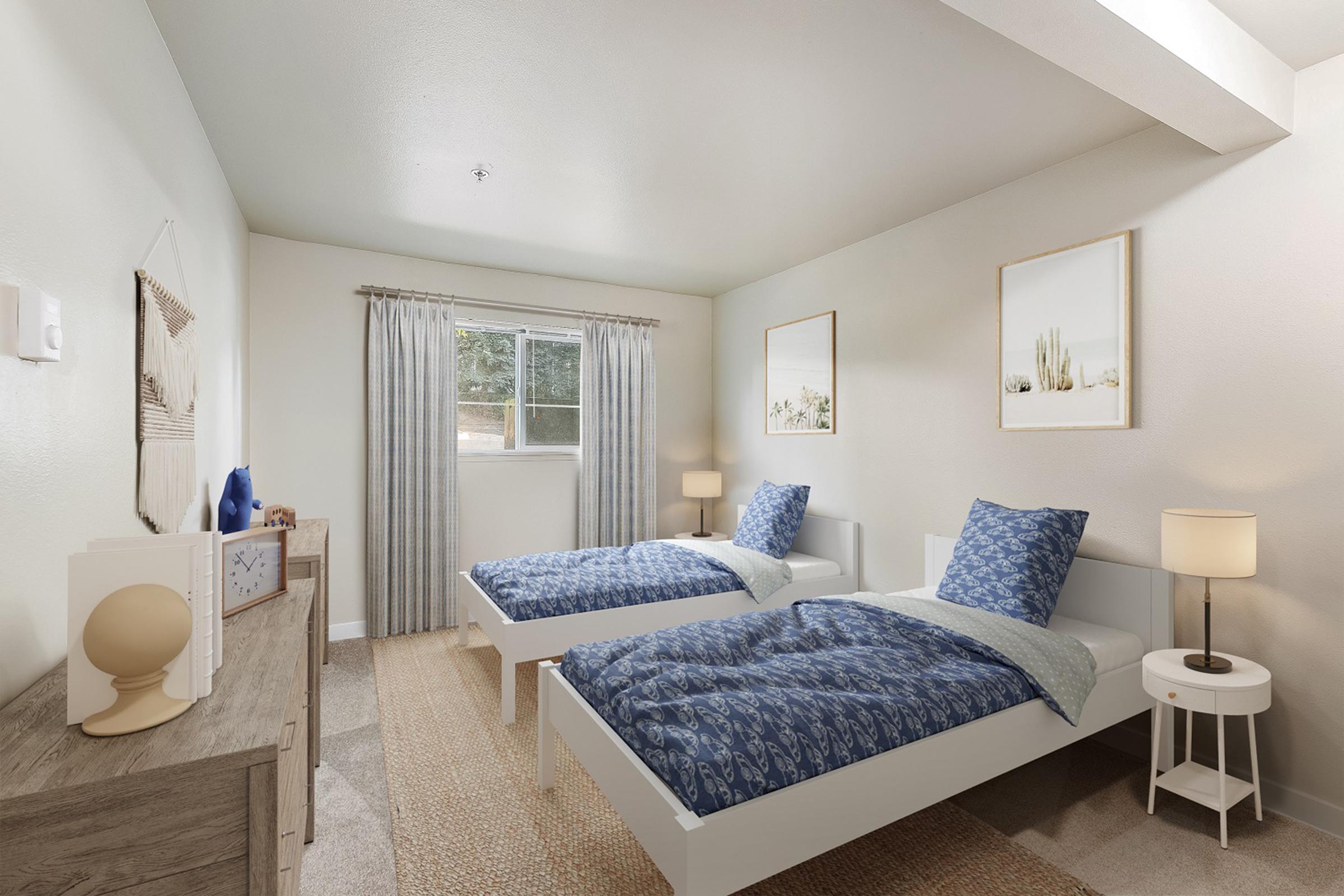 A well-lit bedroom featuring two twin beds with blue patterned beddings. There are light-colored walls, a window with sheer curtains, and two framed artworks. A nightstand with a lamp is beside each bed, and a dresser with decorative items is against one wall, all contributing to a cozy and inviting atmosphere.