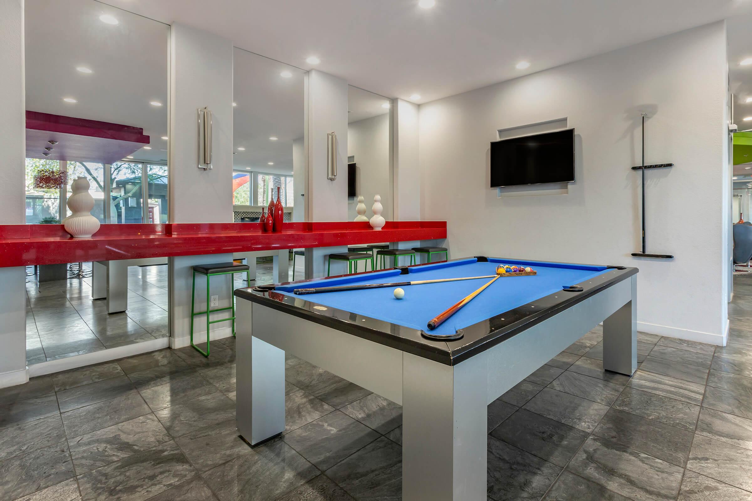 A bright game room featuring a blue pool table with balls, surrounded by modern decor.