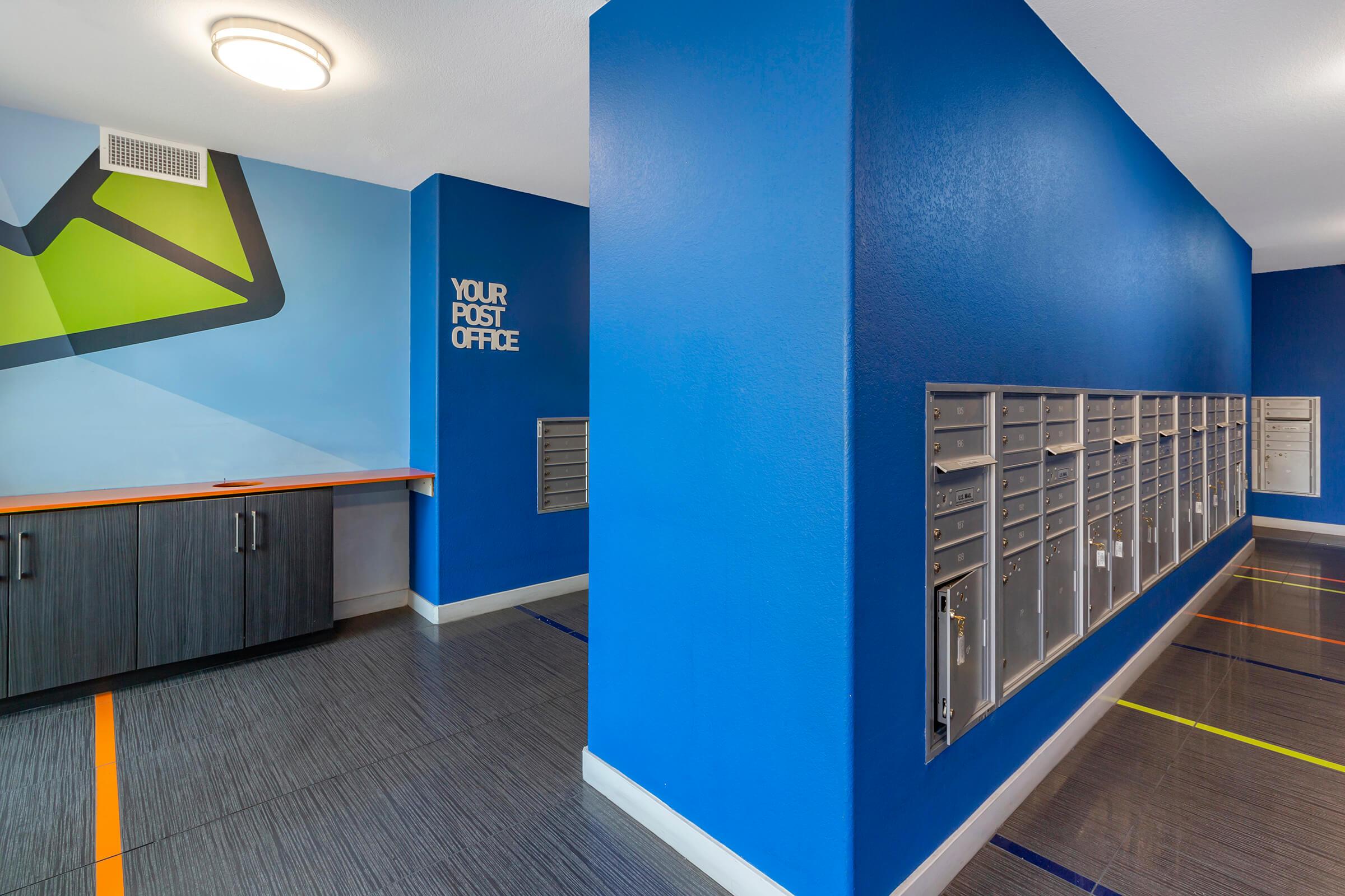 Interior view of a brightly colored post office with blue walls. On the right, there are multiple mailboxes arranged in a row.