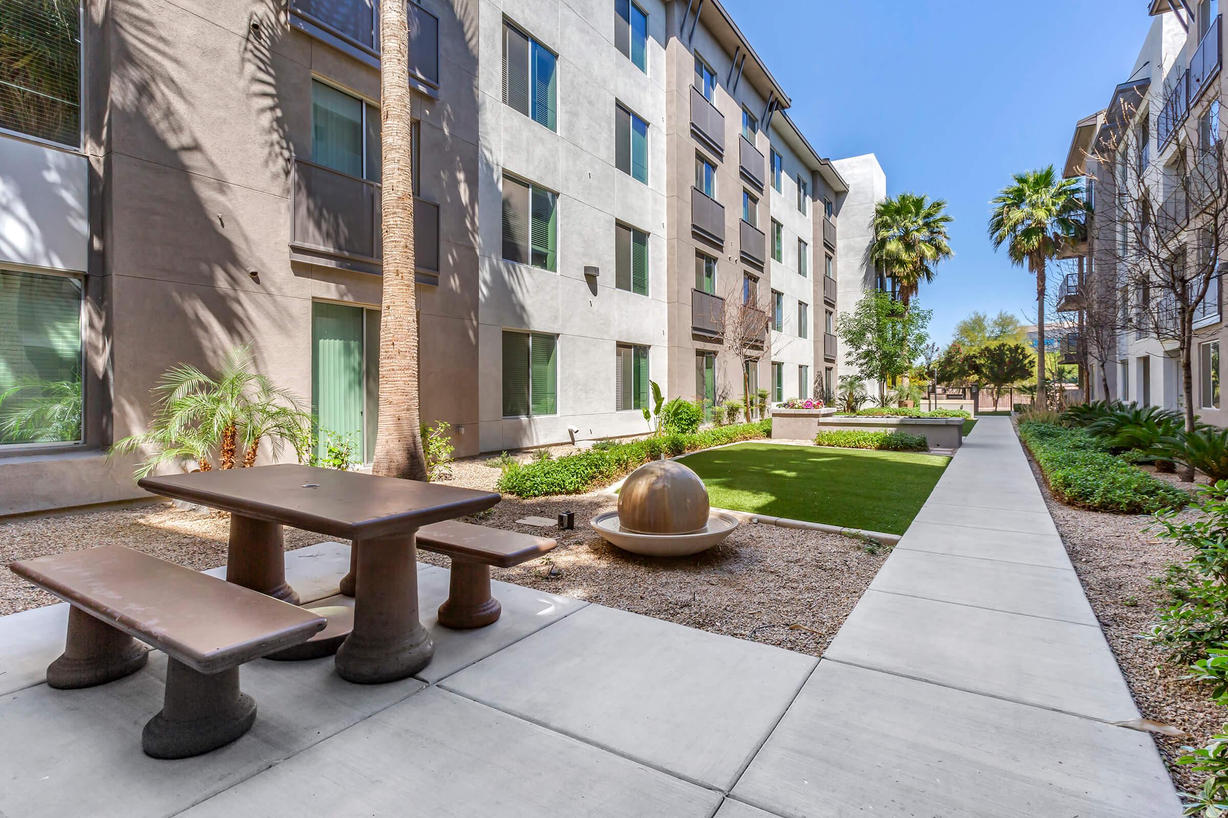 A landscaped courtyard featuring a grassy area, palm trees, and modern buildings.