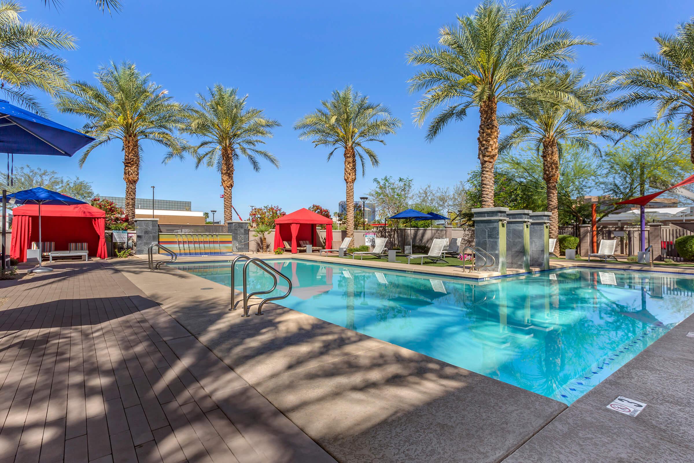 A tranquil outdoor pool area surrounded by tall palm trees, featuring colorful cabanas in red and blue.