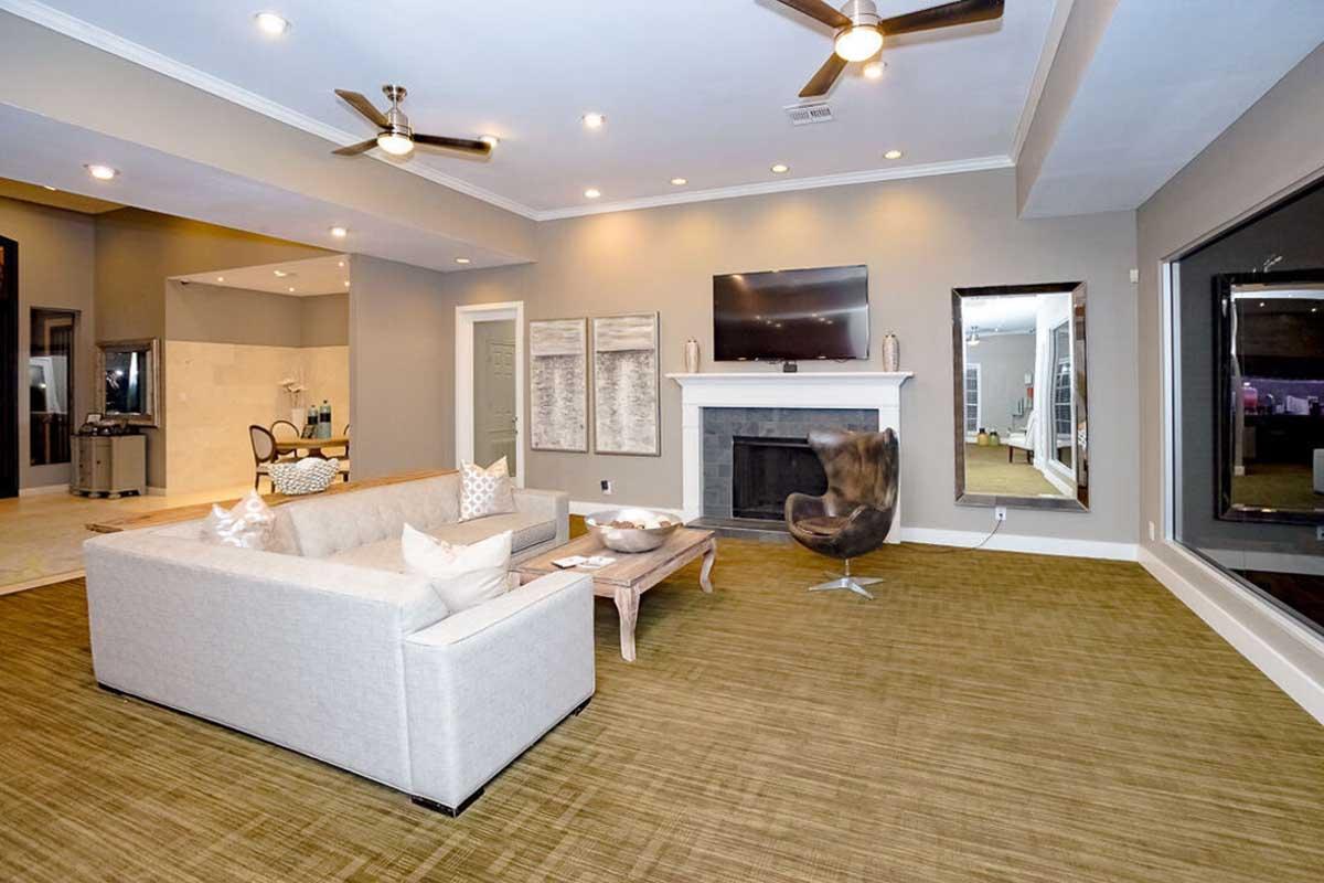 Modern living room featuring a comfortable gray sectional sofa with decorative pillows, a sleek coffee table, and a stylish chair. The space includes a flat-screen TV mounted above a fireplace, large windows for natural light, and neutral wall colors, creating a contemporary and inviting atmosphere.
