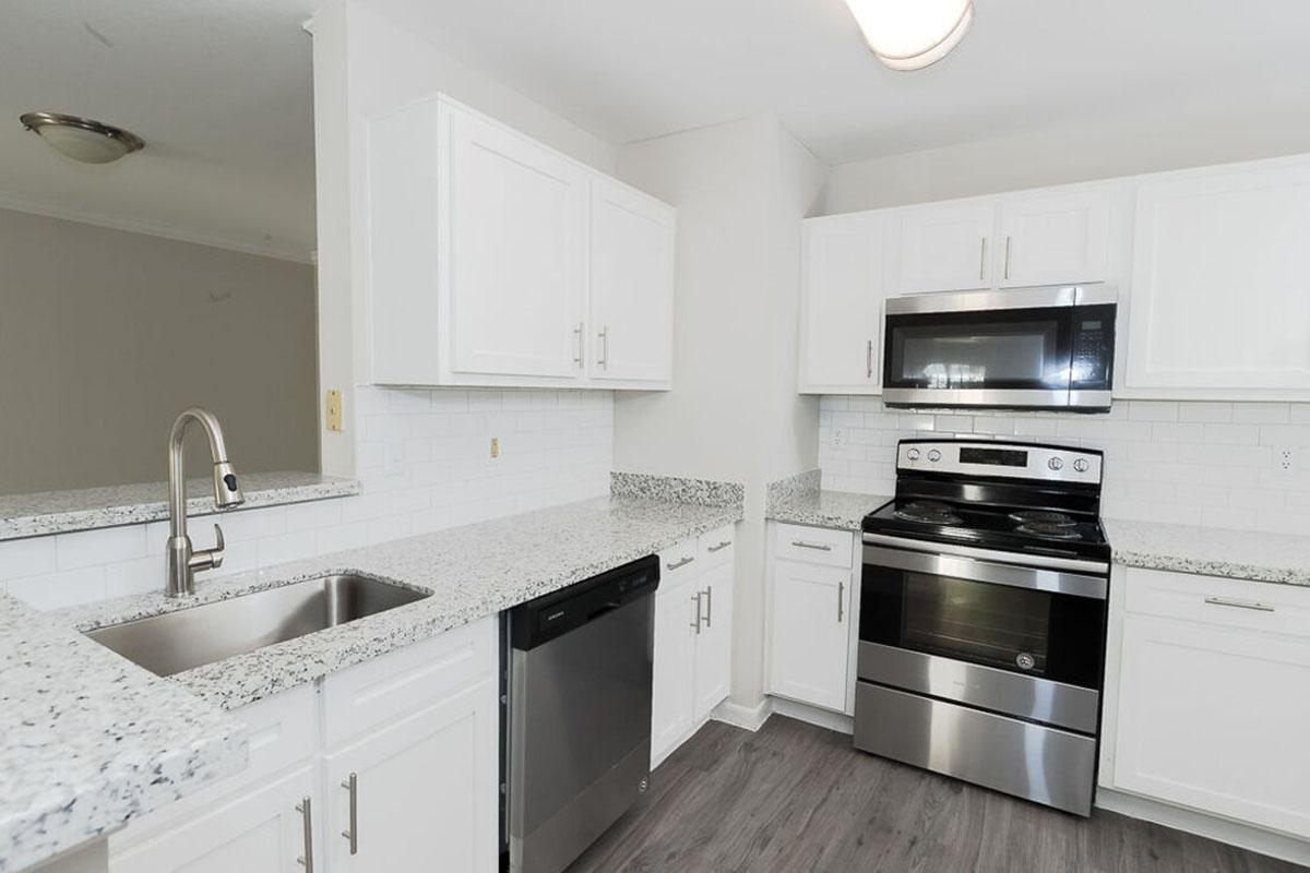 Modern kitchen featuring white cabinetry, granite countertops, stainless steel appliances including an oven, microwave, and dishwasher, with a sleek faucet installed in the sink area. Light-colored flooring complements the overall contemporary design.