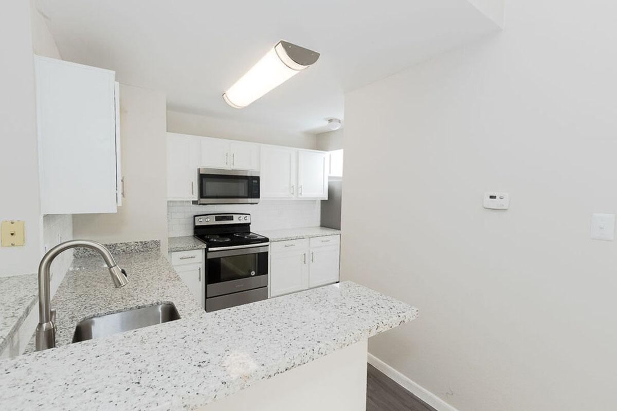Modern kitchen featuring white cabinetry, granite countertops, and stainless steel appliances. Includes a sink with a brushed nickel faucet, an electric stove, and a microwave. The overall design is bright and inviting with natural light coming from a window.