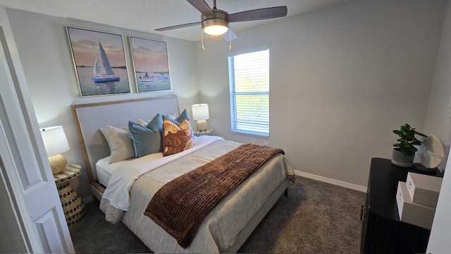A serene bedroom featuring a bed with decorative pillows and a cozy throw. Two bedside lamps illuminate the space, and a fan spins above. Wall art with sailboat themes adds a nautical touch. A window allows natural light, and a small plant sits on a dark bedside table, enhancing the room's inviting atmosphere.