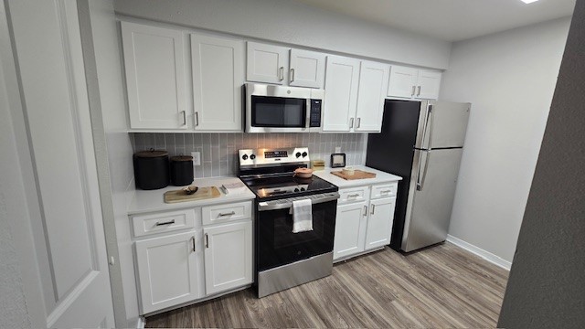 Modern kitchen design featuring white cabinetry, stainless steel appliances including a microwave and refrigerator, a black stove, and a light-toned countertop. The space is well-lit, showcasing wooden flooring and a minimalist aesthetic with some decorative items on the counter.