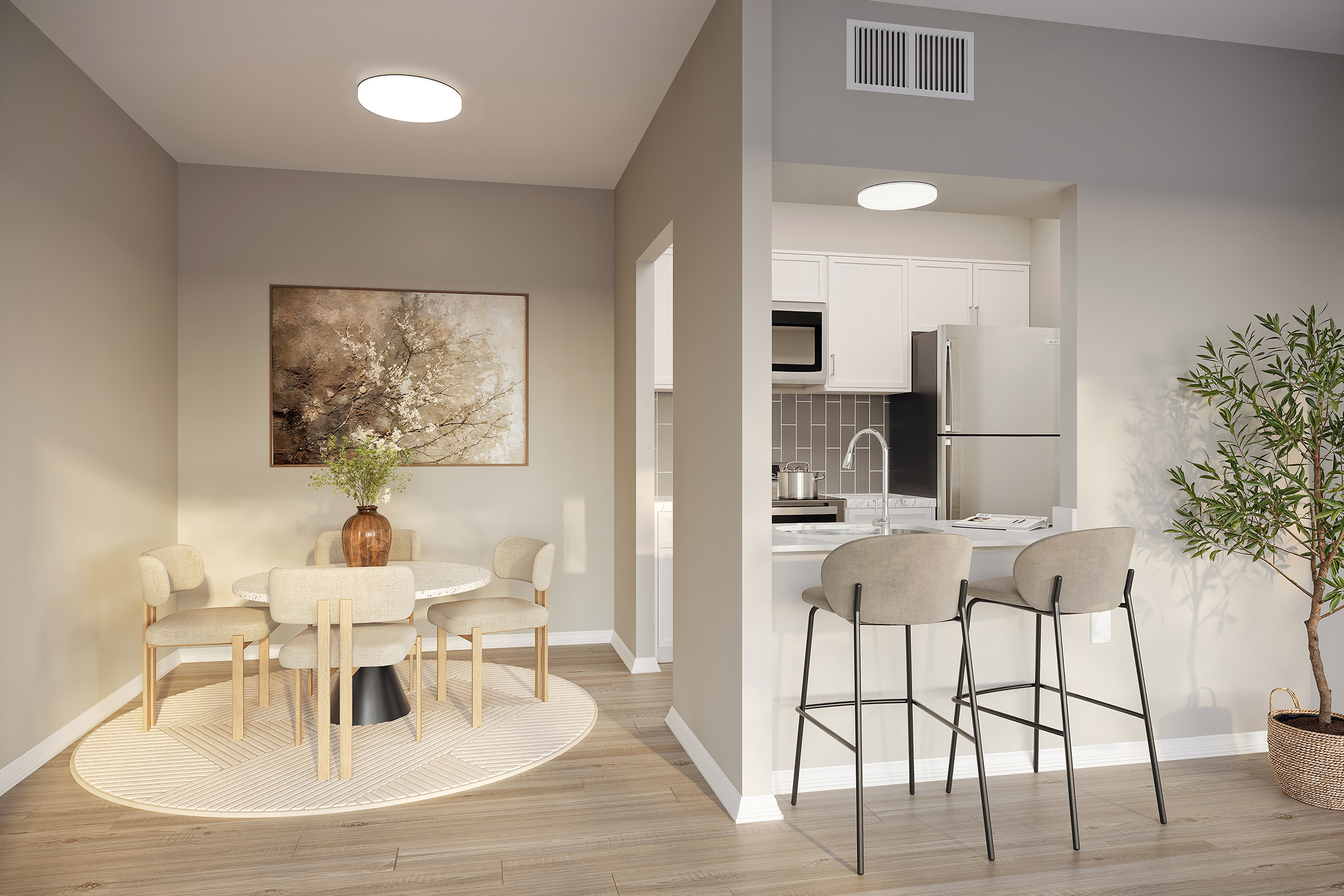 A modern dining area featuring a round table with four chairs, set on a circular rug. Adjacent is a kitchen area with a stainless steel fridge and microwave. The space is well-lit with a ceiling light and includes a decorative plant and artwork on the wall, creating a warm, inviting atmosphere.