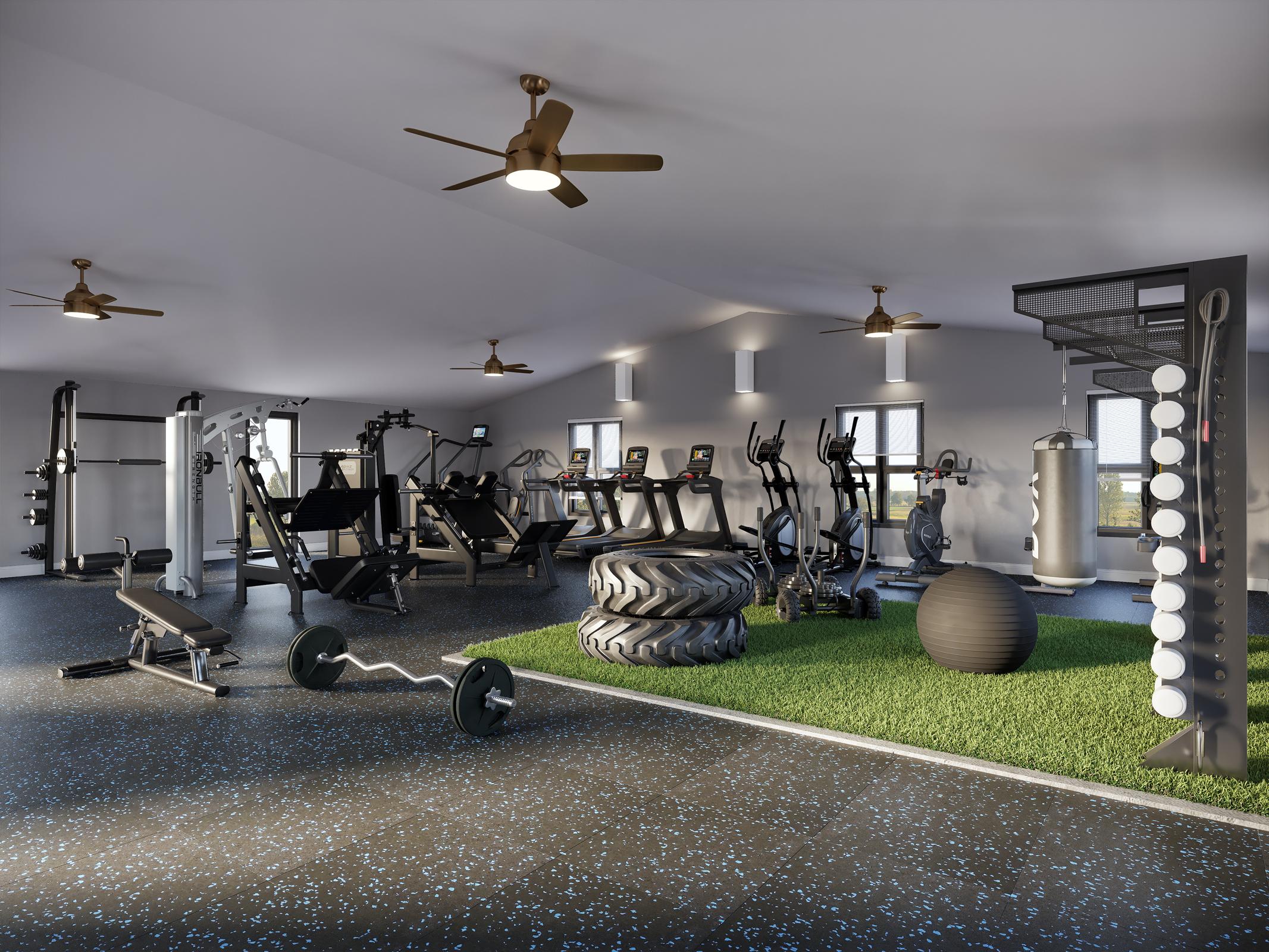 A modern gym interior featuring various exercise equipment, including weight machines, treadmills, and free weights. The space has a rubber floor with blue specks, green turf, and overhead ceiling fans, providing a bright and open atmosphere for workouts. Large windows allow natural light to fill the room.