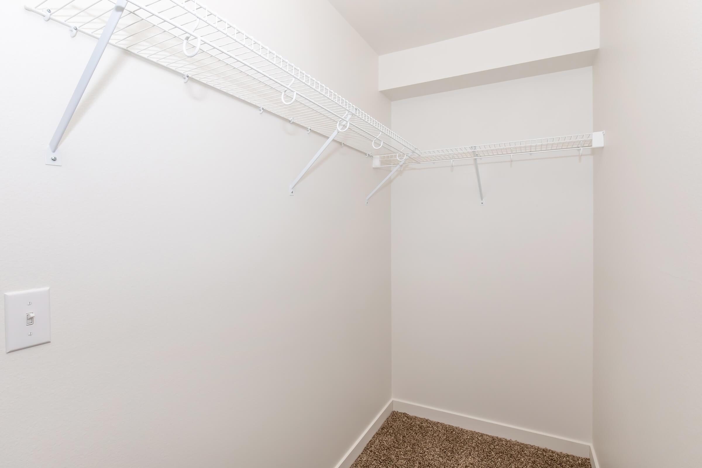 A small, empty closet featuring white wire shelving installed on the wall. The walls are plain and the floor is covered with a light brown carpet. The closet appears organized and ready for storage.