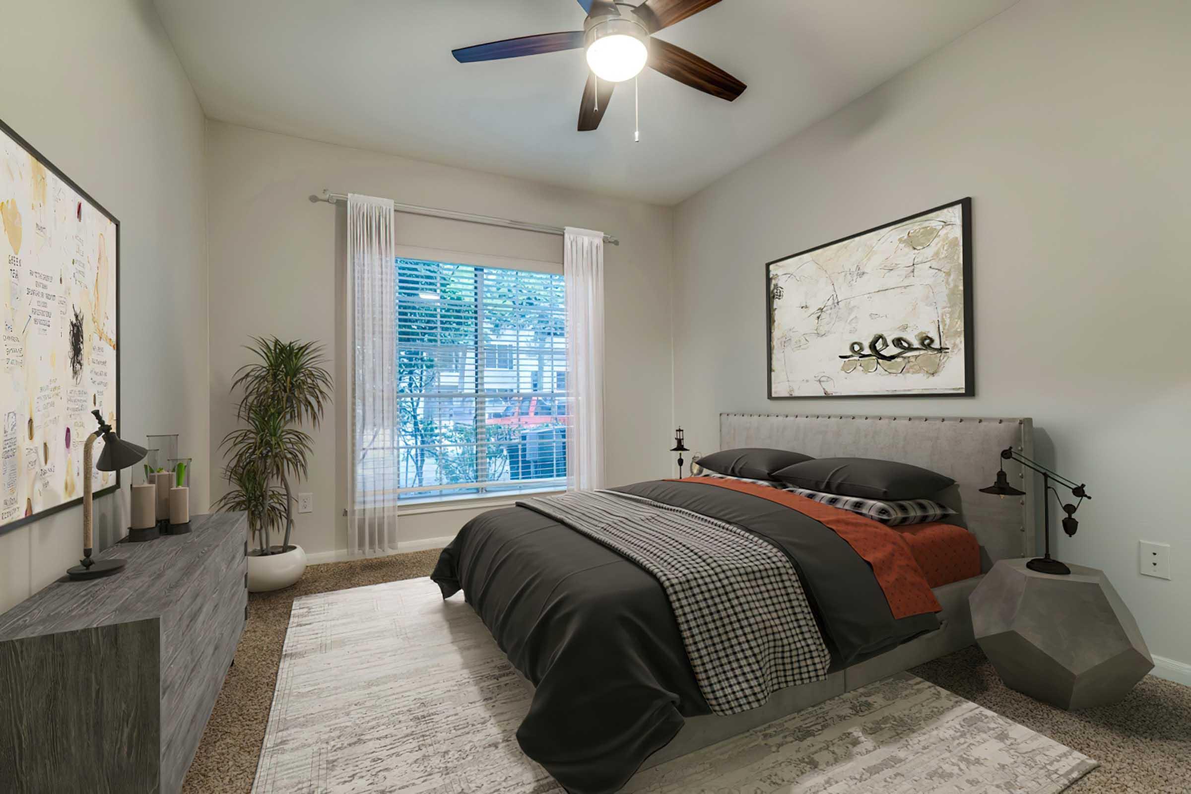 A cozy bedroom featuring a gray upholstered bed with black and red bedding, modern light fixtures, and a decorative wall art piece. A textured area rug is on the floor, complemented by a stylish nightstand and a potted plant. Natural light filters through a window with white curtains.