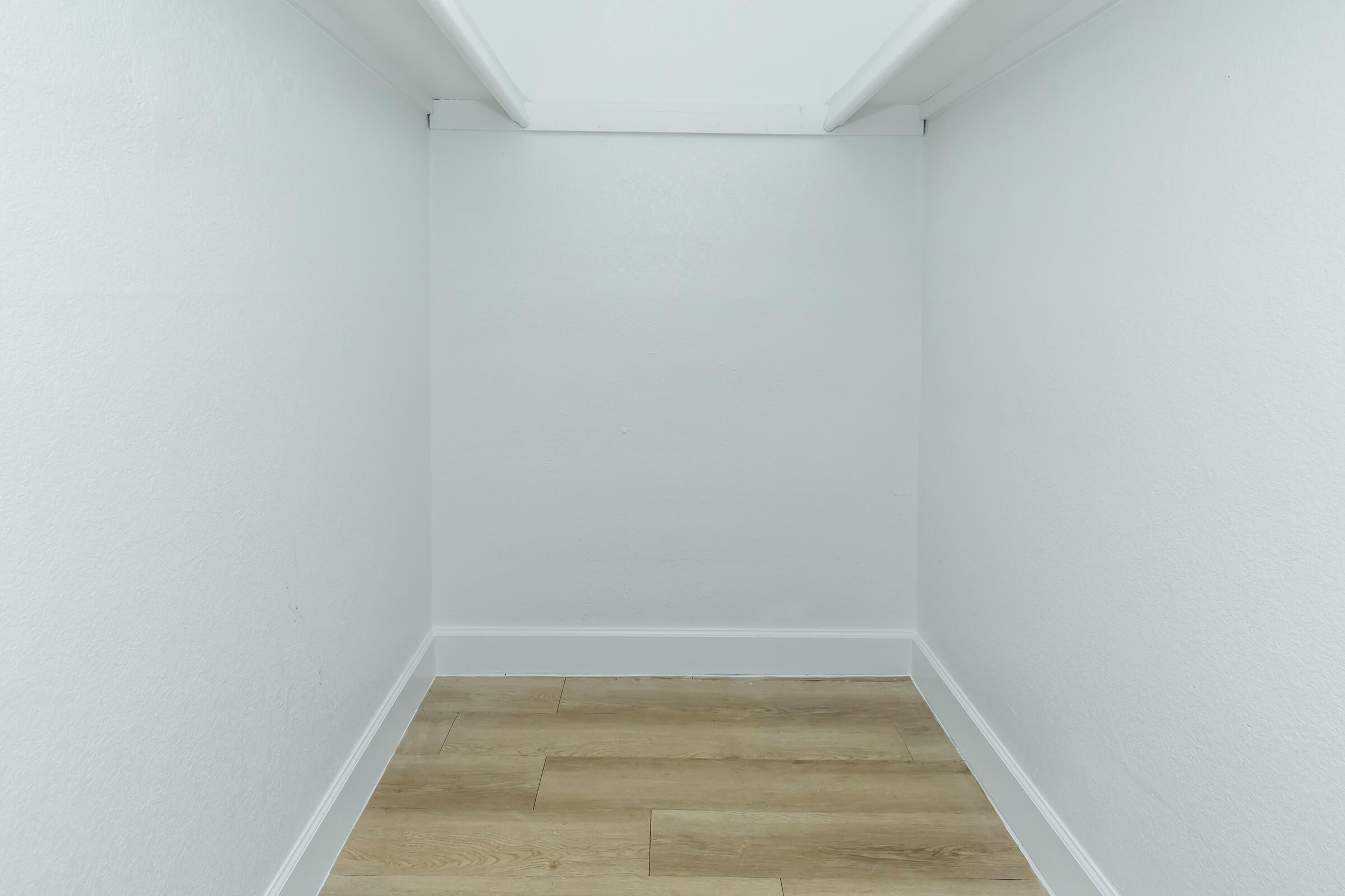 Empty interior of a small room or closet with white walls and light wooden flooring, featuring a simple, minimalist design. The space is unoccupied, suggesting potential for storage or use.