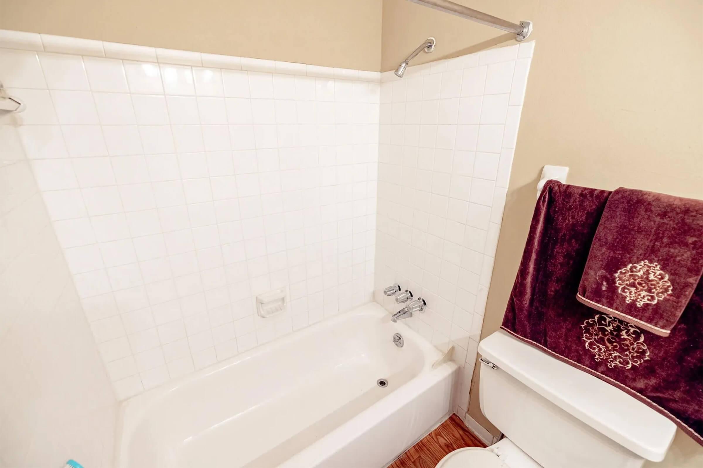 A clean bathroom featuring a bathtub with a shower curtain, a chrome faucet, and a white toilet. A plush, deep burgundy towel hangs on a rack next to the bathtub, complementing the neutral-colored walls and tiled floor.