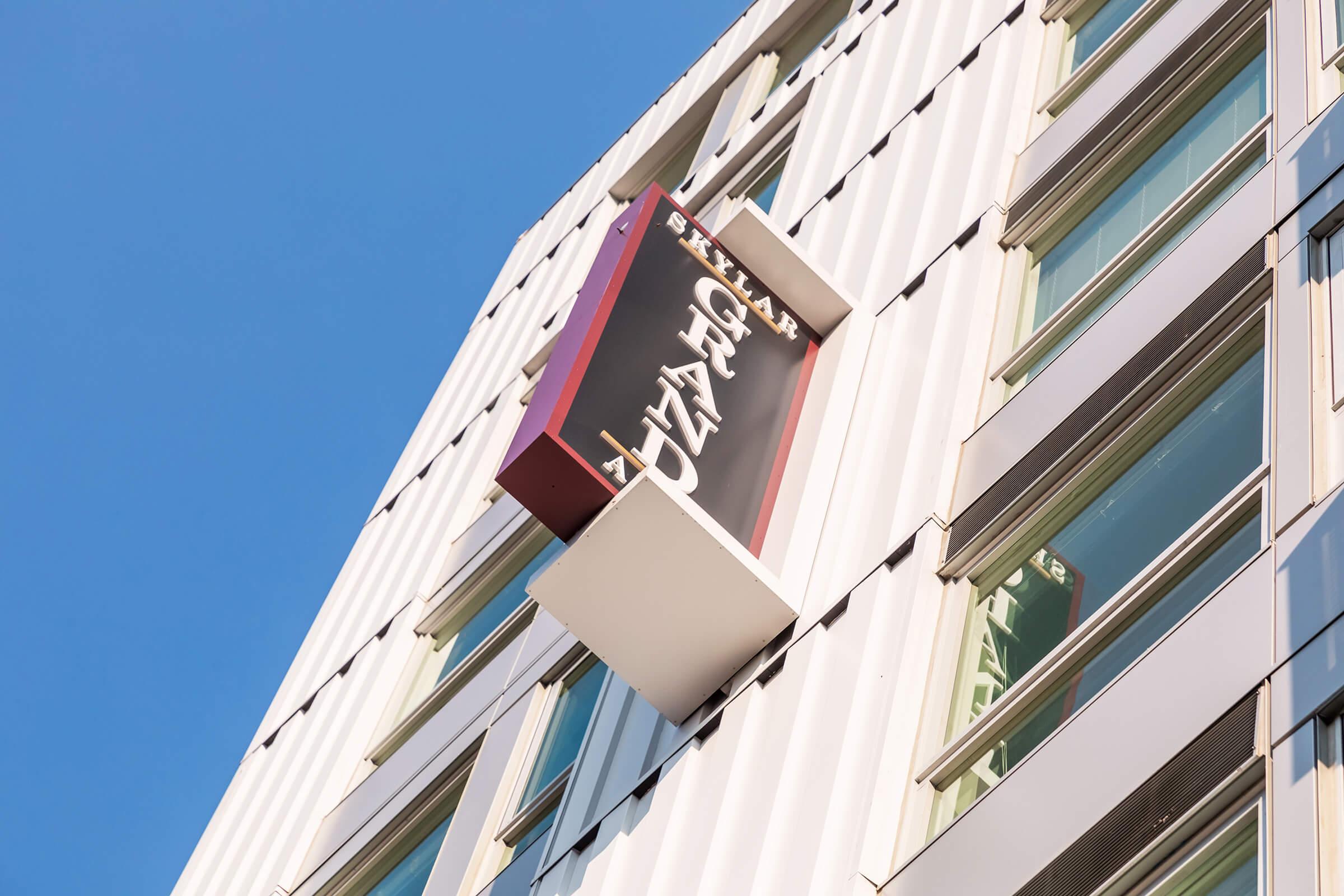 Signage for "Grand" attached to a modern building, with a clear blue sky in the background. The letters are bold and stylized, set against a bright red and white background. The building features large glass windows, showcasing a contemporary architectural design.