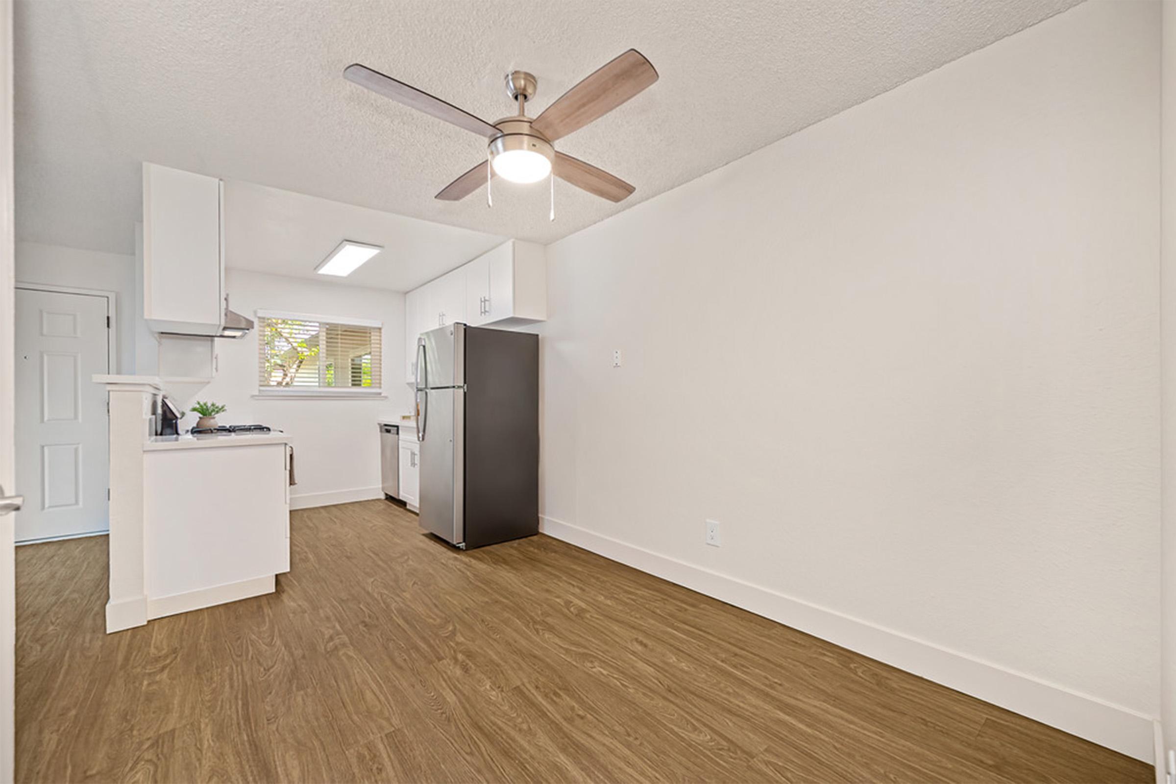 A modern kitchen featuring white cabinetry and a stainless steel refrigerator. The space has light-colored walls, wood-style flooring, and a ceiling fan. A window allows natural light to brighten the area, creating a bright and airy atmosphere.