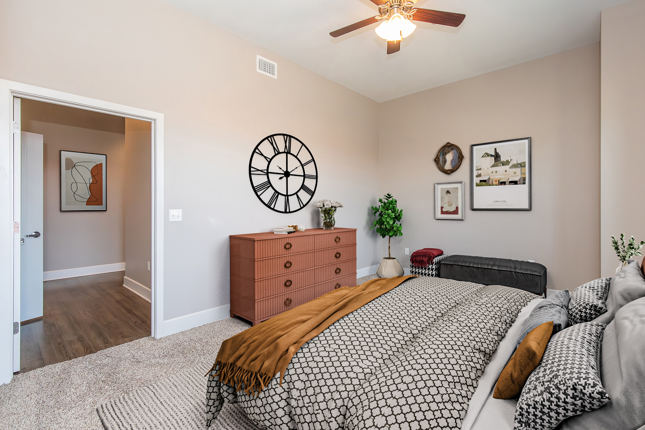 A serene bedroom featuring a bed with a stylish gray and gold bedding set. A large wall clock and framed artwork adorn the walls. A wooden dresser with decorative items sits beside the bed, while a cozy chair and an open door lead to a hallway, creating an inviting atmosphere.