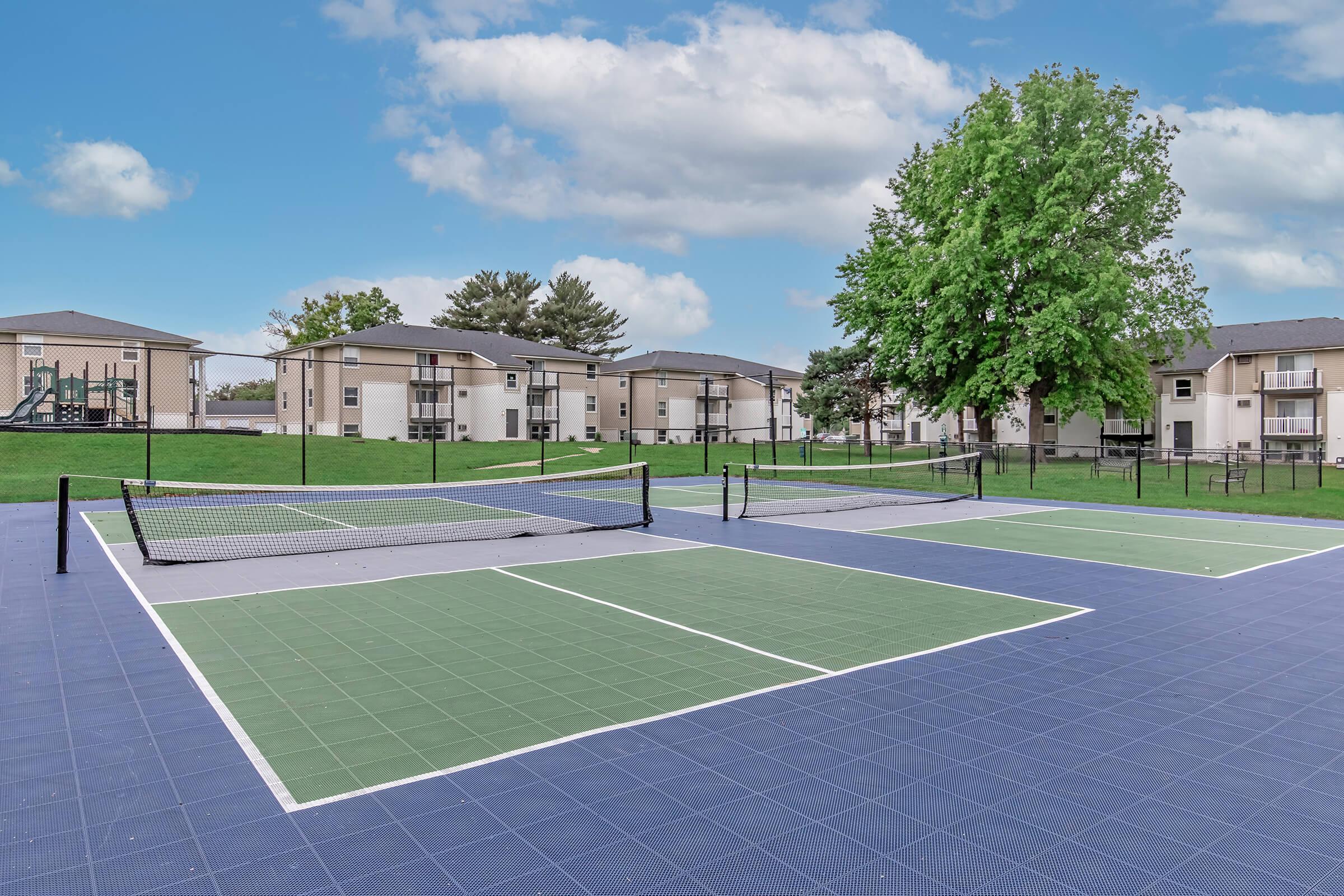 Full-size tennis court with fencing and blue surface in Bexley’s amenity-rich Urbandale apartment community.