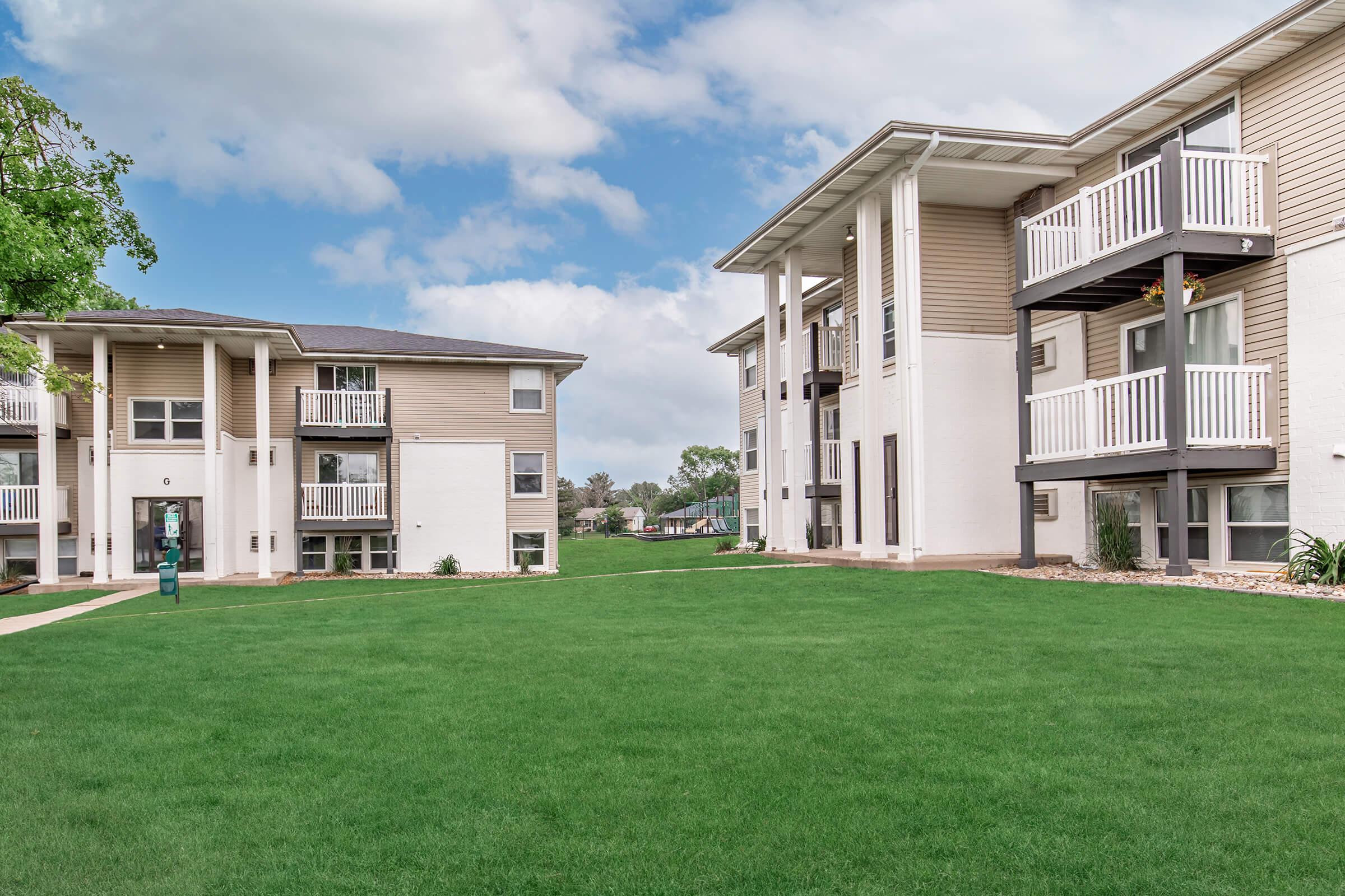 Wide-angle view of two Bexley apartment buildings with lawn and mature trees.