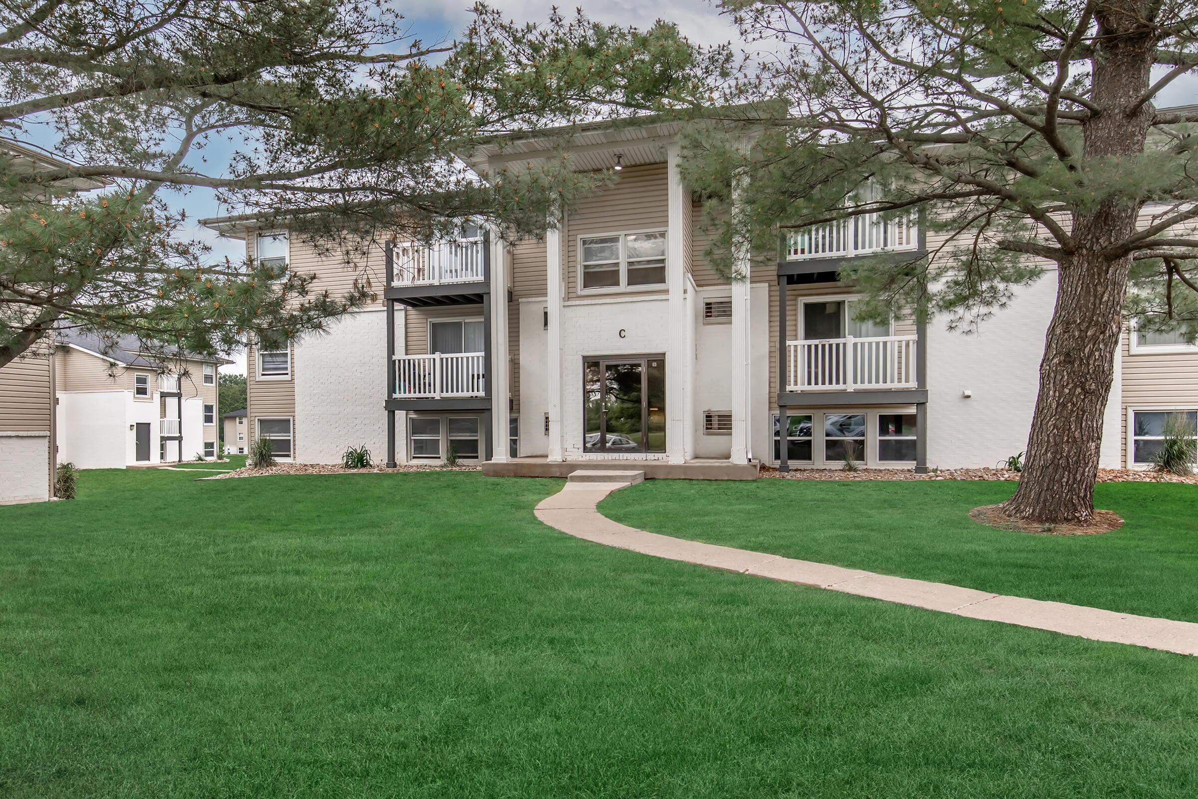 Front-facing exterior of Bexley Apartments with well-maintained lawn and tall pine trees.