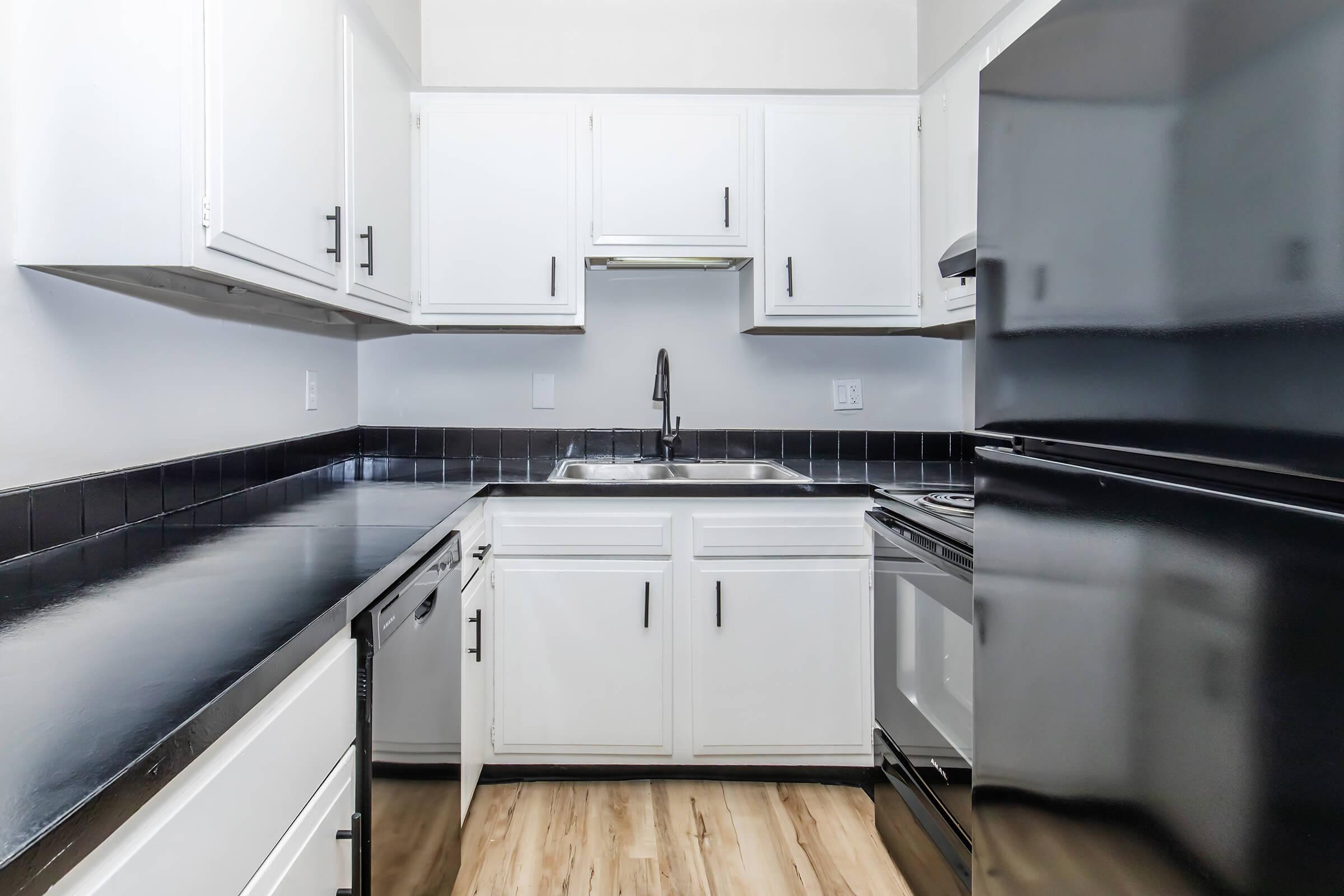 Renovated galley kitchen with white cabinets, black countertops, stainless steel sink, and dishwasher.