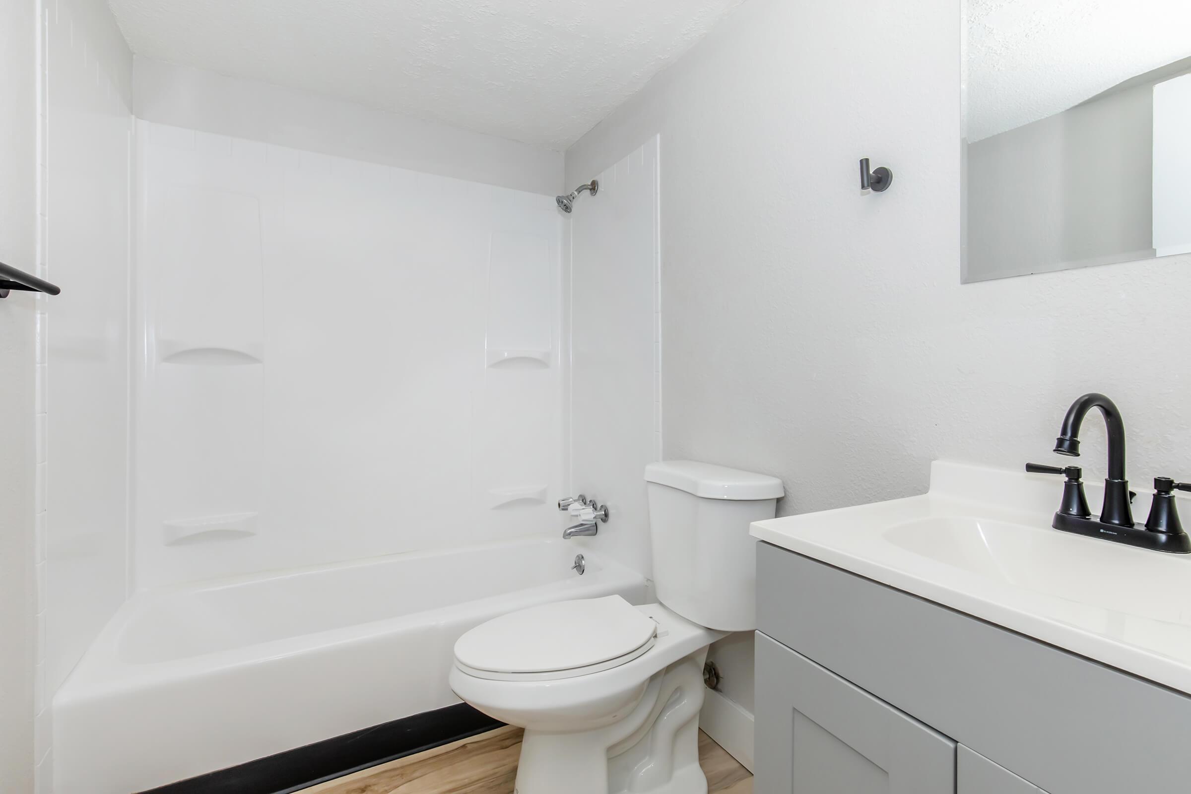 Renovated bathroom with full tub, white vanity, black fixtures, and modern lighting at Bexley Apartments.
