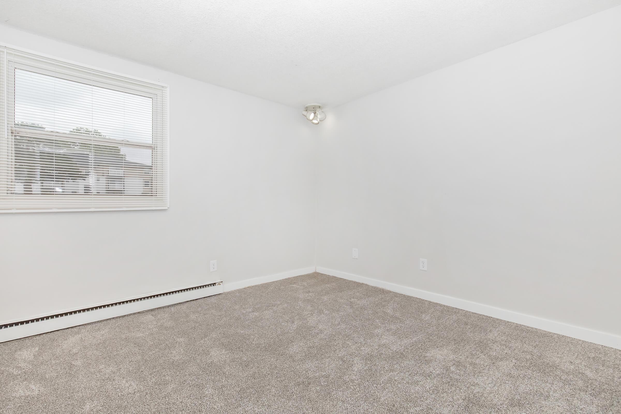 Corner view of carpeted bedroom with baseboard heater and natural light in Bexley Urbandale 1-bedroom.