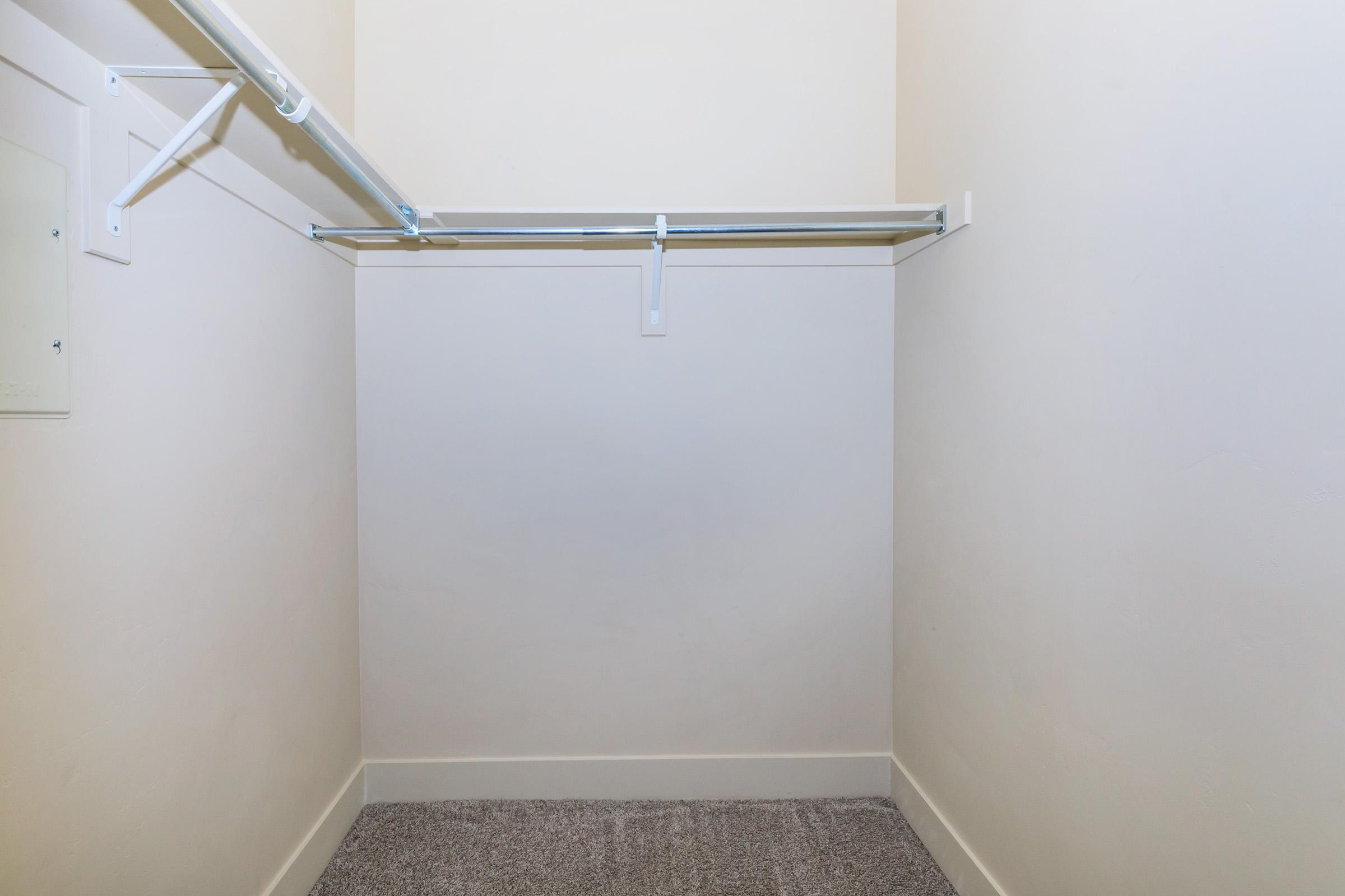 Empty closet with a light-colored wall, a single hanging rod along one side, and carpeted flooring. There are no shelves or items visible, creating a minimalist and spacious appearance.