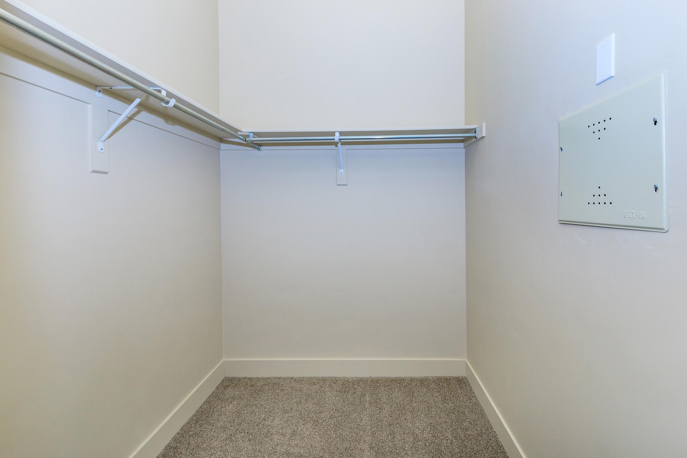 Empty closet with a carpeted floor, featuring two metal hanging rods along the walls and a light-colored wall. No items or storage visible, creating a minimalist and spacious appearance.