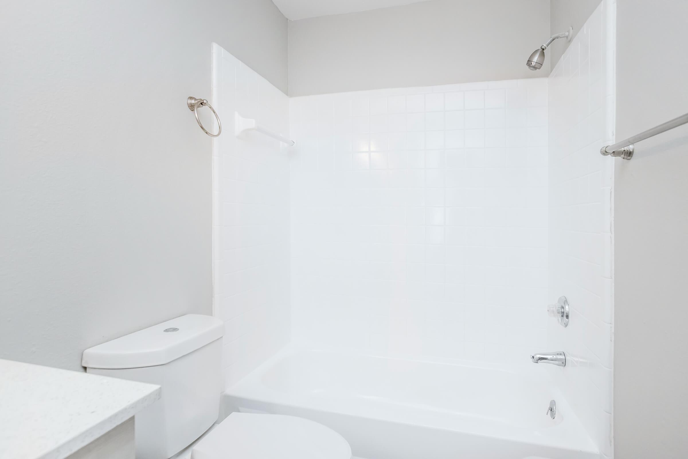 A clean and modern bathroom featuring a white bathtub and shower with a sliding glass door, a white toilet, and light gray walls. The space is well-lit, creating a fresh and bright atmosphere, with simple fixtures and no visible clutter.