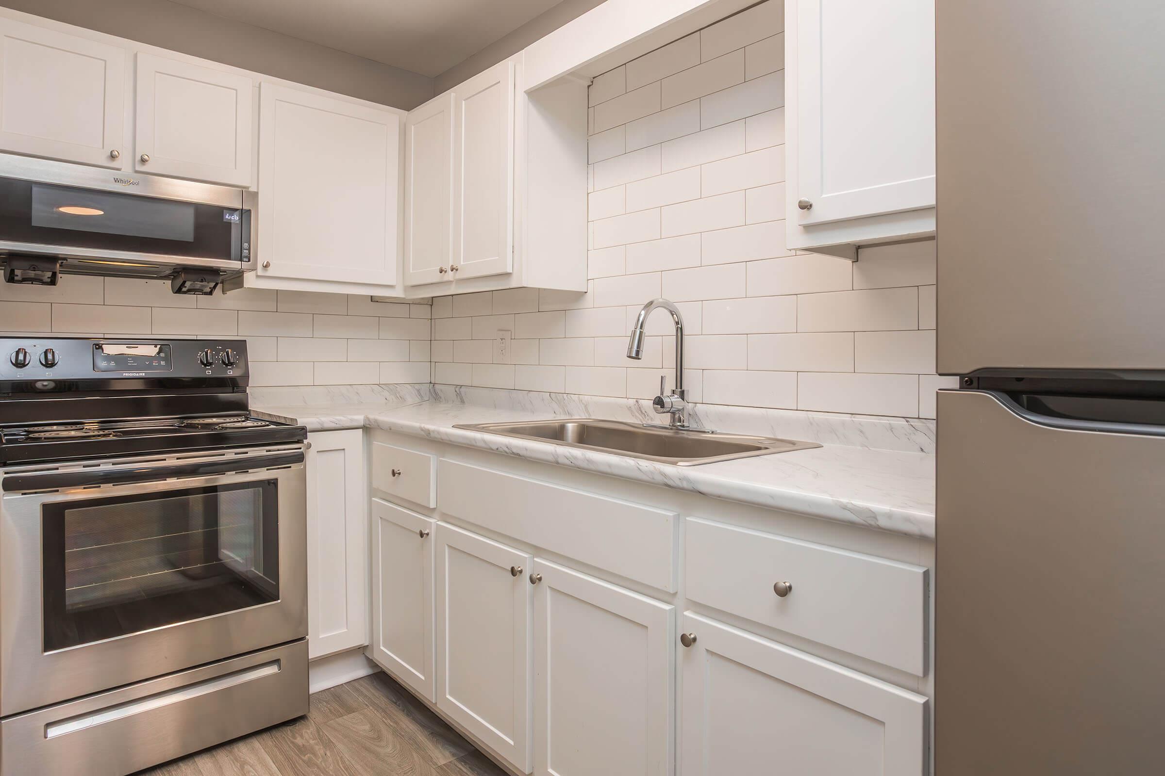 Modern kitchen featuring white cabinetry, a stainless steel oven and refrigerator, and a double basin sink with a polished marble countertop. The backsplash consists of white subway tiles, enhancing the bright and clean aesthetic of the space. Natural light illuminates the area, creating a welcoming atmosphere.