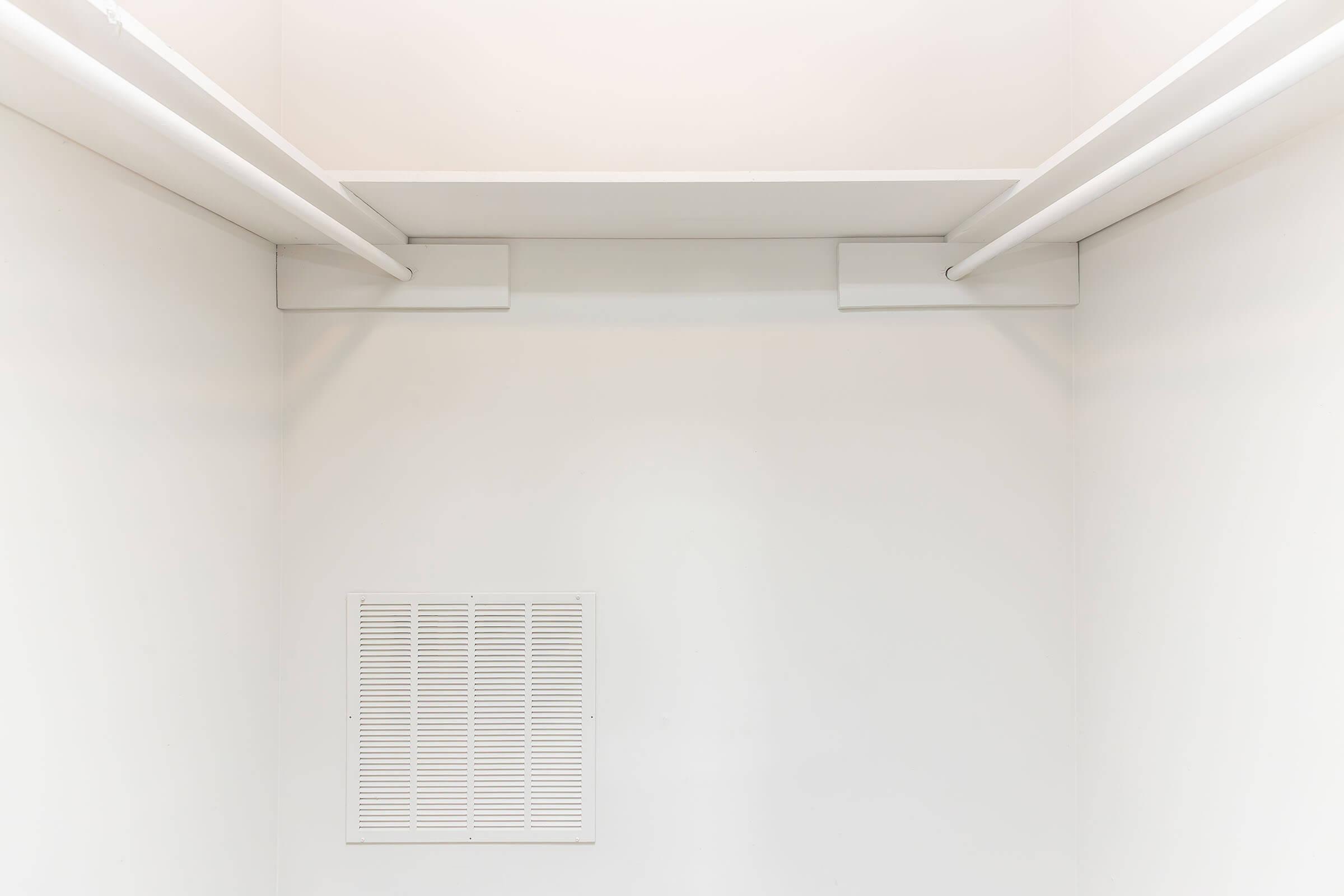 A minimalistic, empty closet featuring two horizontal clothing rods and a vent on the wall. The walls and ceiling are painted white, giving the space a clean and open appearance. No items or decorations are visible, emphasizing the simplicity of the design.