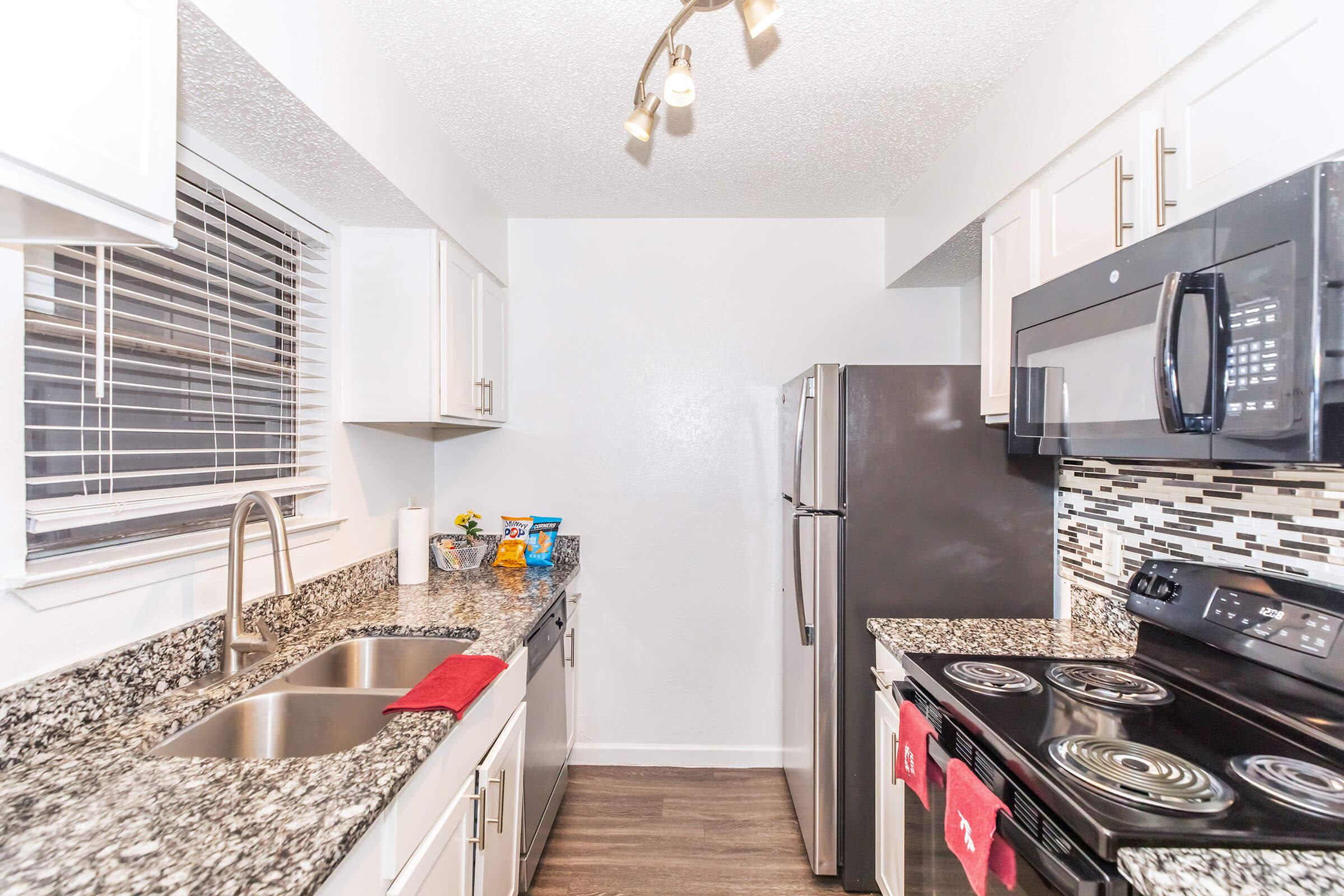 Modern kitchen showcasing white cabinetry, granite countertops, stainless steel appliances including a refrigerator and oven, and a sleek black microwave. The space features a double sink with a stylish faucet and a backsplash with decorative tiles. Soft lighting enhances the inviting atmosphere.