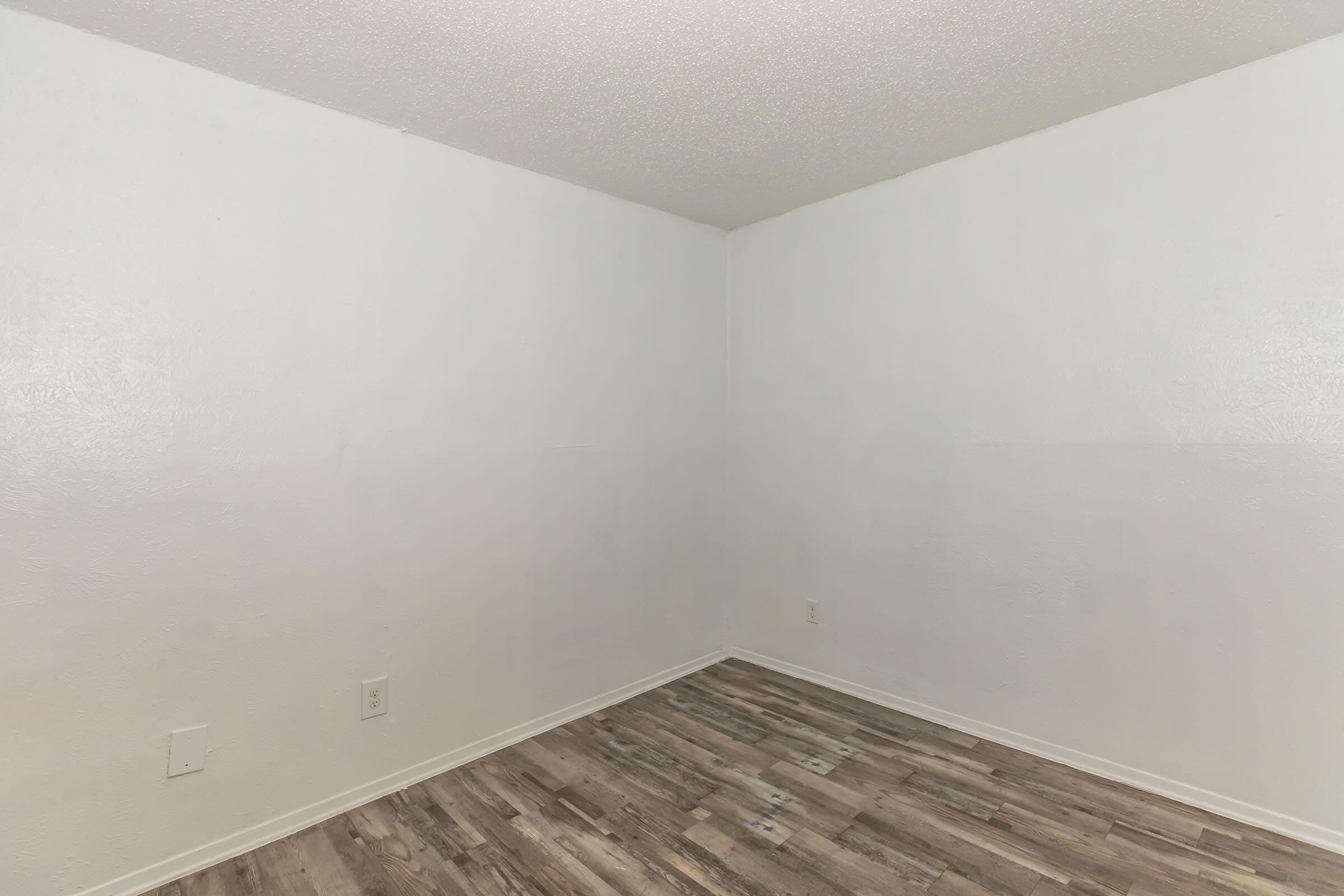 Empty room with white walls and a light-colored wooden floor. The space is devoid of furniture or decor, creating a minimalist atmosphere. The walls appear smooth, and there is a light texture on the surface, while the flooring consists of planks arranged in a horizontal pattern.