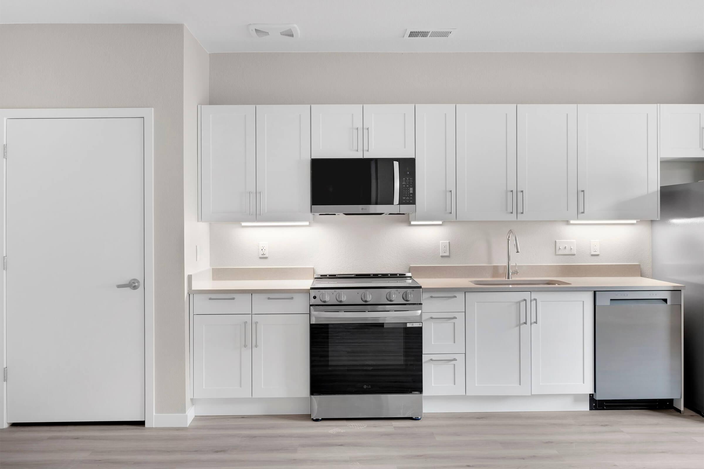 Modern kitchen featuring white cabinetry, a stainless steel oven and microwave, a sink, and a silver refrigerator. Light-colored walls and flooring create a bright, spacious atmosphere.