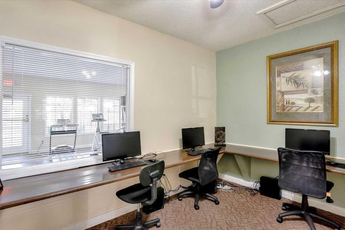 A small office space featuring two computer stations with ergonomic chairs, a framed artwork on the wall, and a large window providing natural light. The room is well-organized, with a neutral color scheme and a clean, professional atmosphere.
